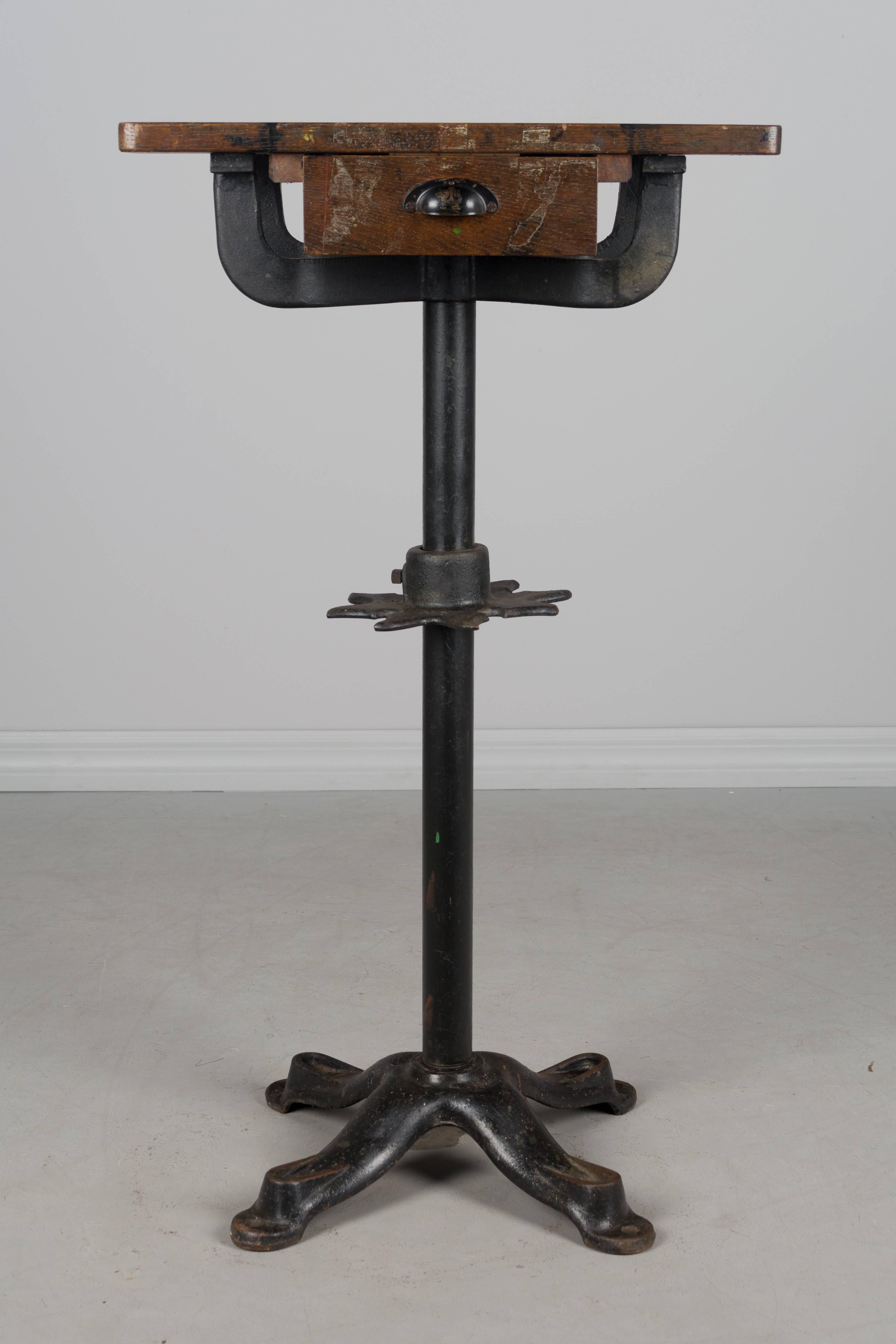 19th century French Industrial work table with cast iron pedestal base. Oak top with one dovetailed drawer. Nice old patina to the wood with black stains and paint residue. A decorative star-shaped cast iron piece on the pole has notches to hold