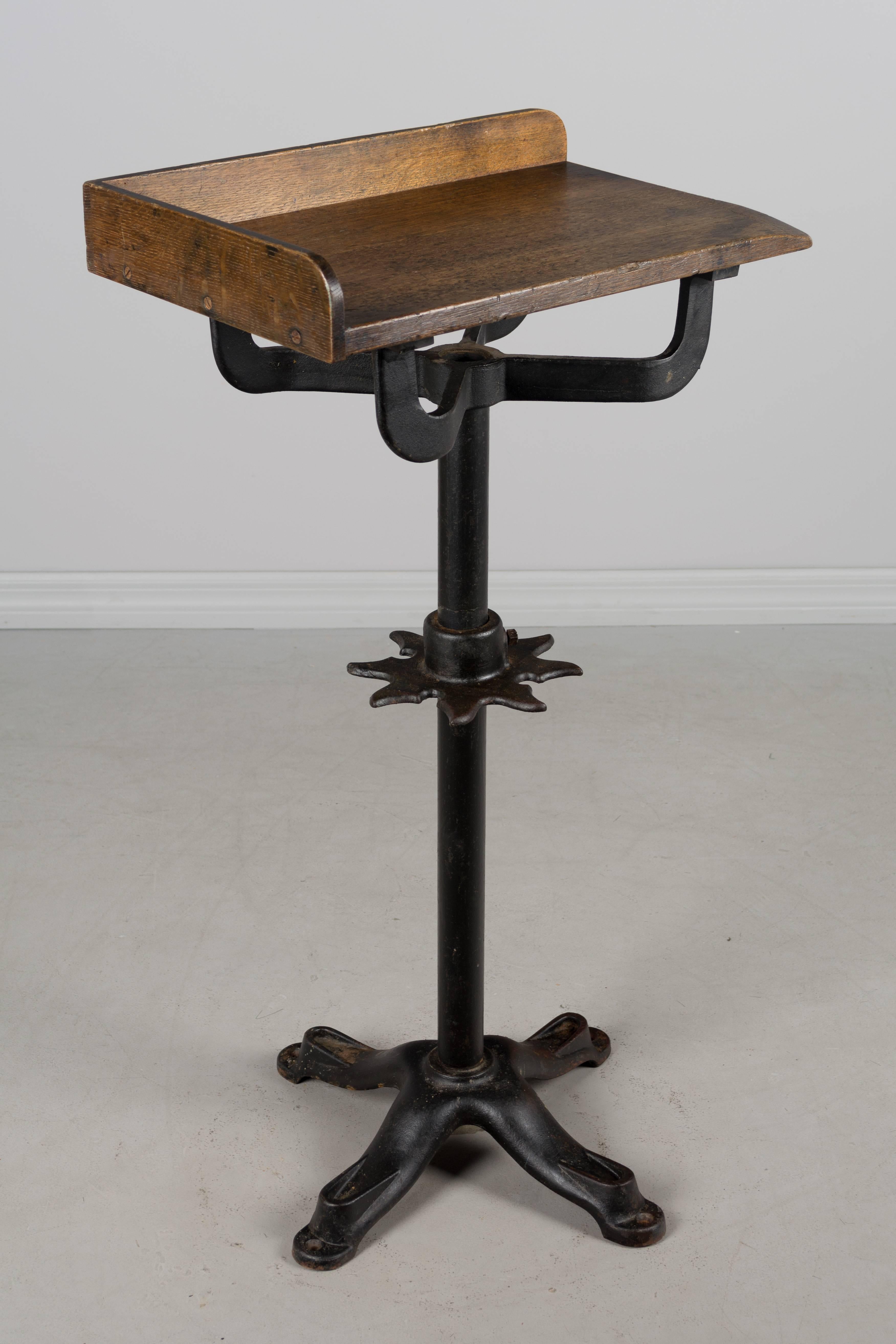 19th century French Industrial work table with cast iron pedestal base. Oak top with worn surface in the corner. Waxed patina. A decorative star-shaped cast iron piece on the pole has notches to hold tools and is adjustable with one bolt holding it