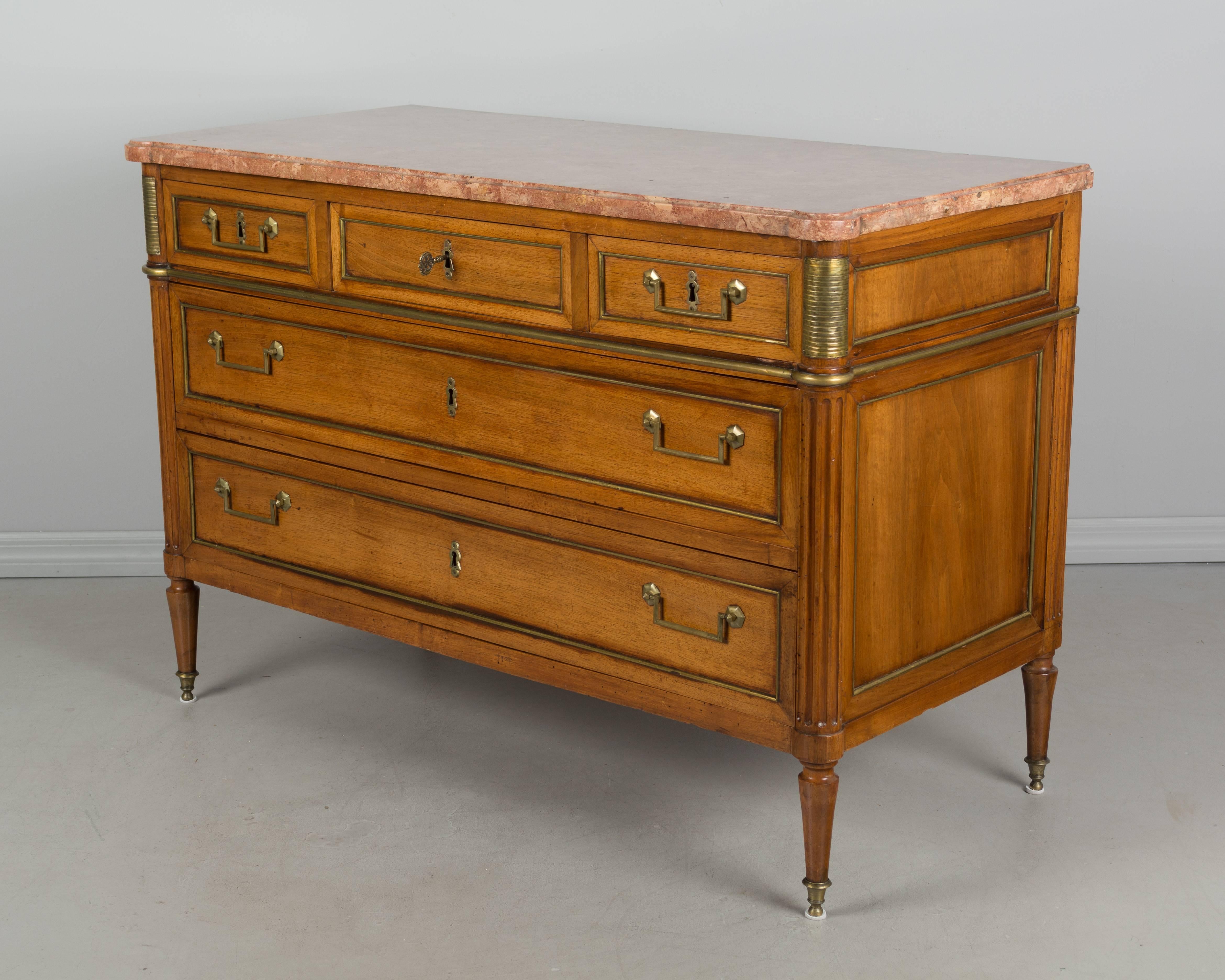 An excellent French Louis XVI style walnut commode. Five dovetailed drawers with brass decoration and original pulls. Five locks in working order with one key. Original marble top. Great construction and nicely detailed with fluted columns ending in