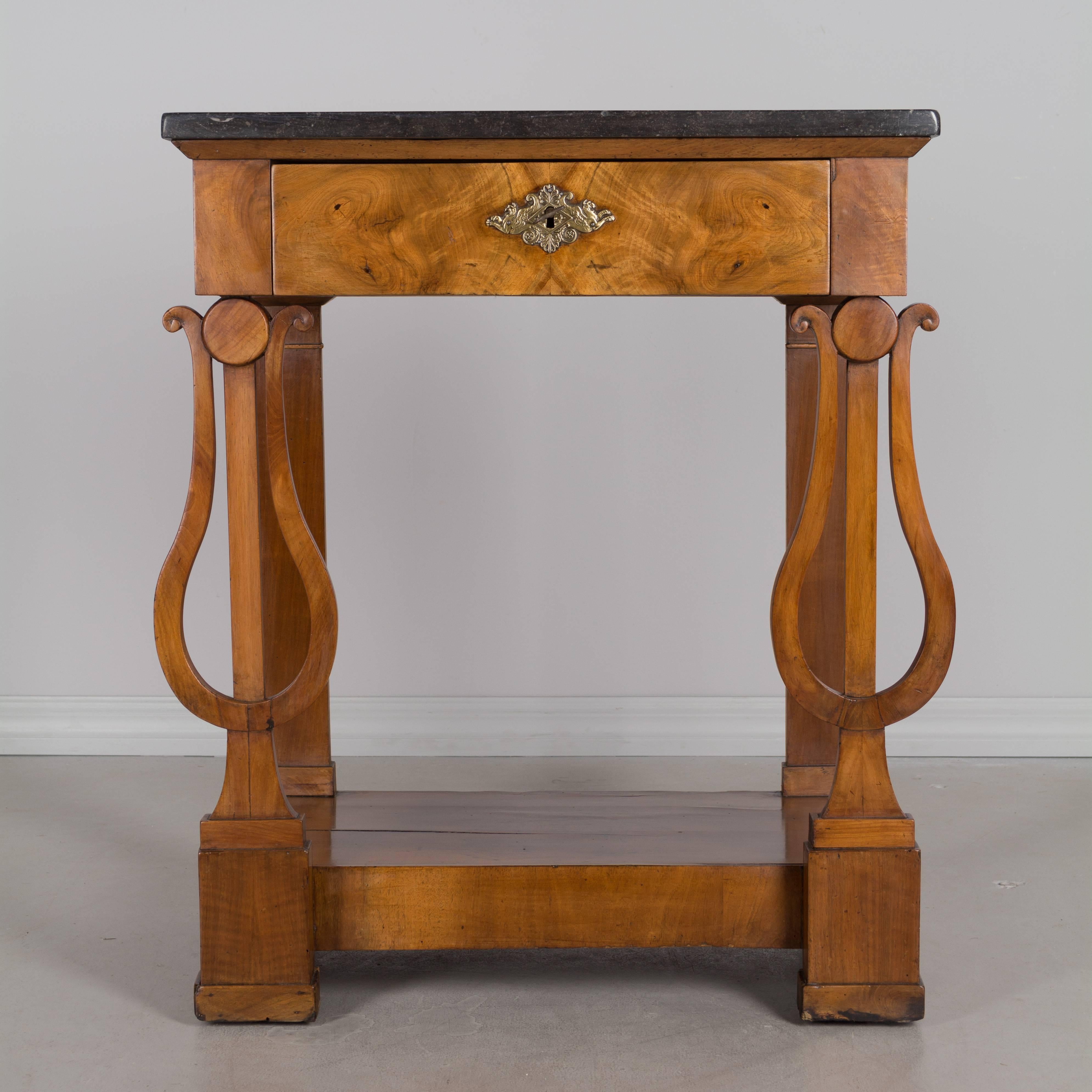 A 19th century French Empire console or side table with original black marble top. Beautifully carved walnut lyre shaped front legs. Dovetailed drawer with bookmatched veneer of walnut. Decorative brass escutcheon with lock and key in working order.