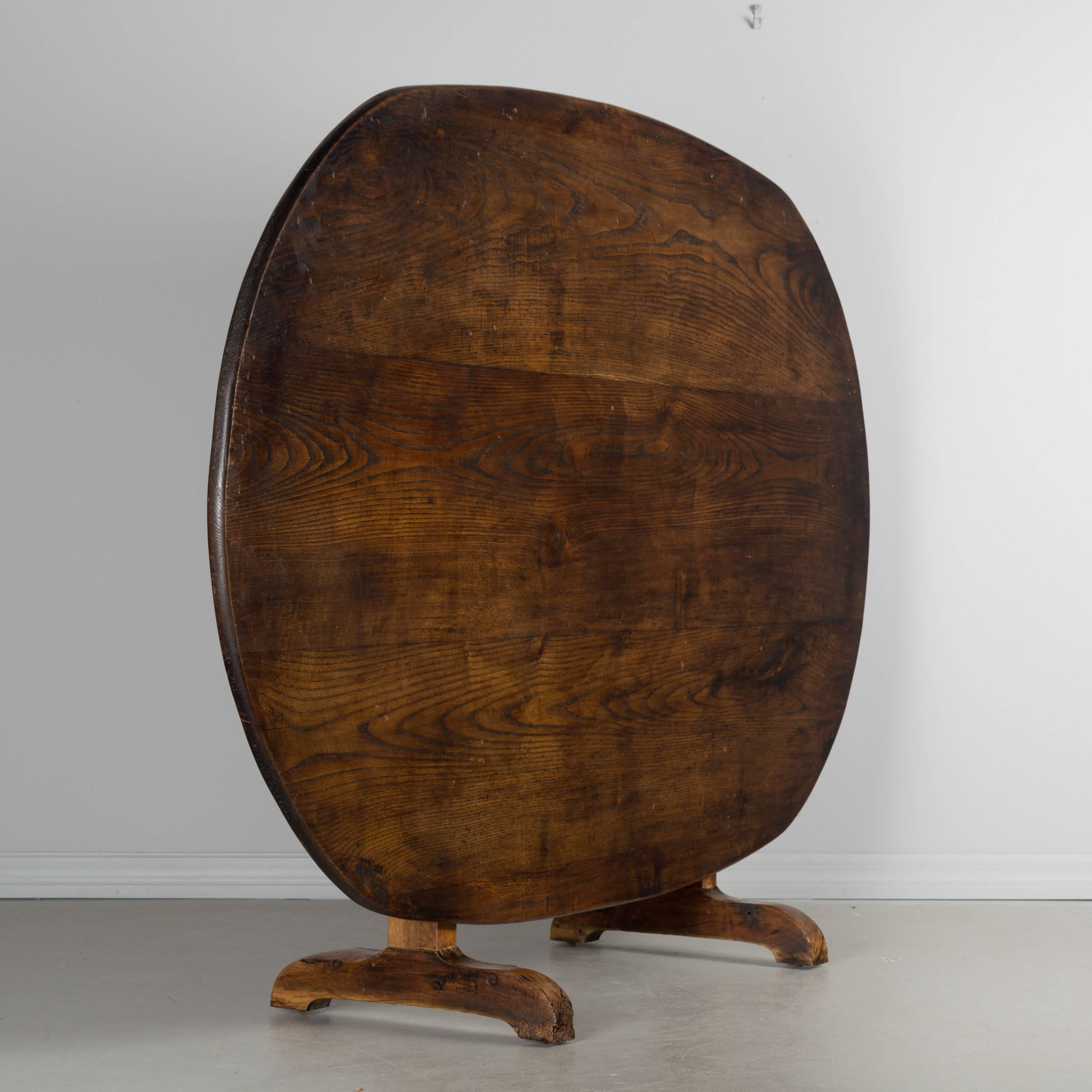 A 19th century French tilt-top table with a large oval top made from wide planks of pine and a study solid walnut base. Waxed finish. Measure: The height when tilted is 52 inches.