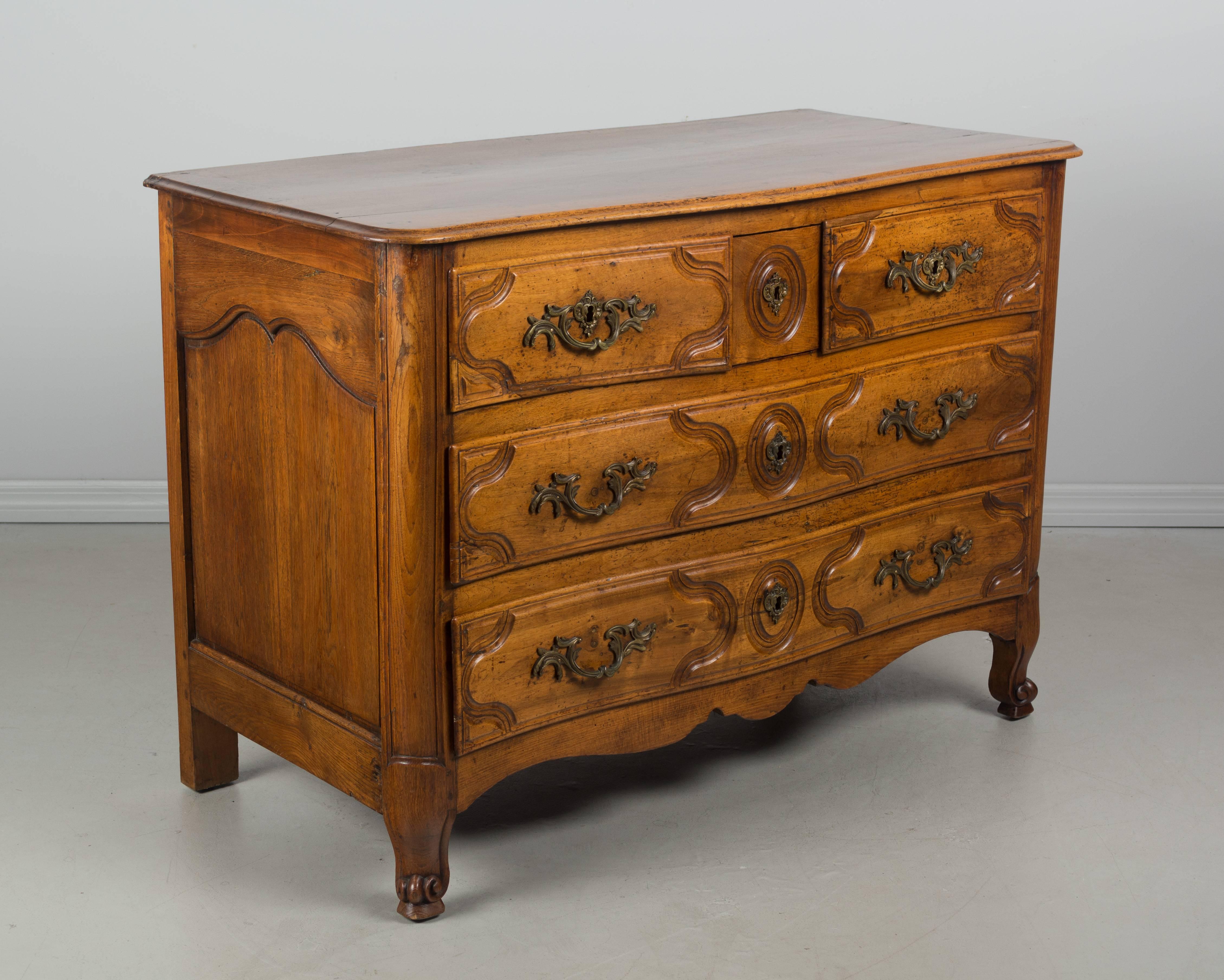 A 19th century French Louis XV style serpentine front commode, or chest of drawers, from Paris. The top and front are made of solid walnut and the sides are made of oak. Dovetailed drawers with hand-carved decoration and brass hardware. Waxed