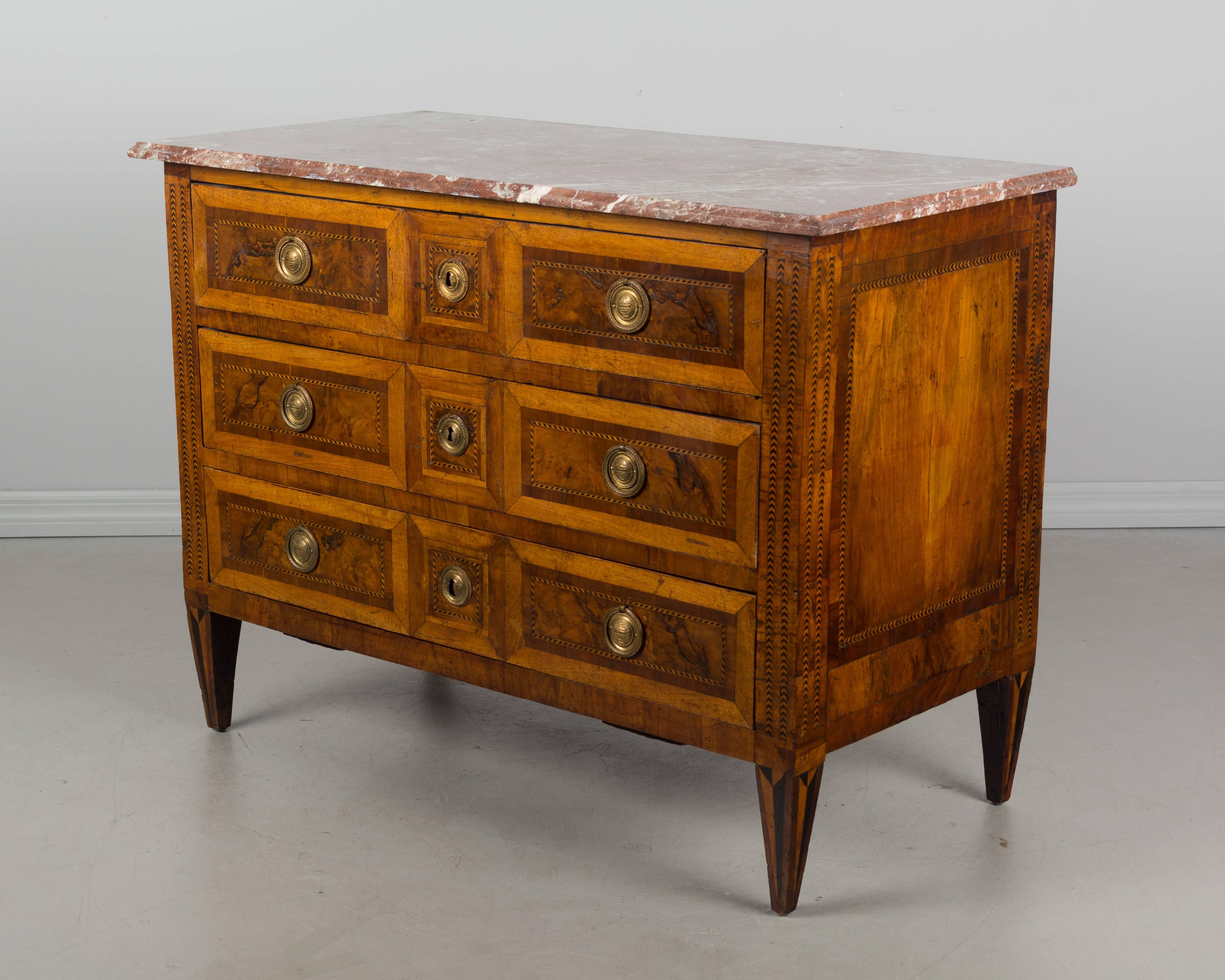 An 18th century Louis XVI marquetry commode with three dovetailed drawers and red veined marble top. Made of veneers of walnut and inlaid with various woods. The hardware is not original to the piece, but is of the same time period. Locks are