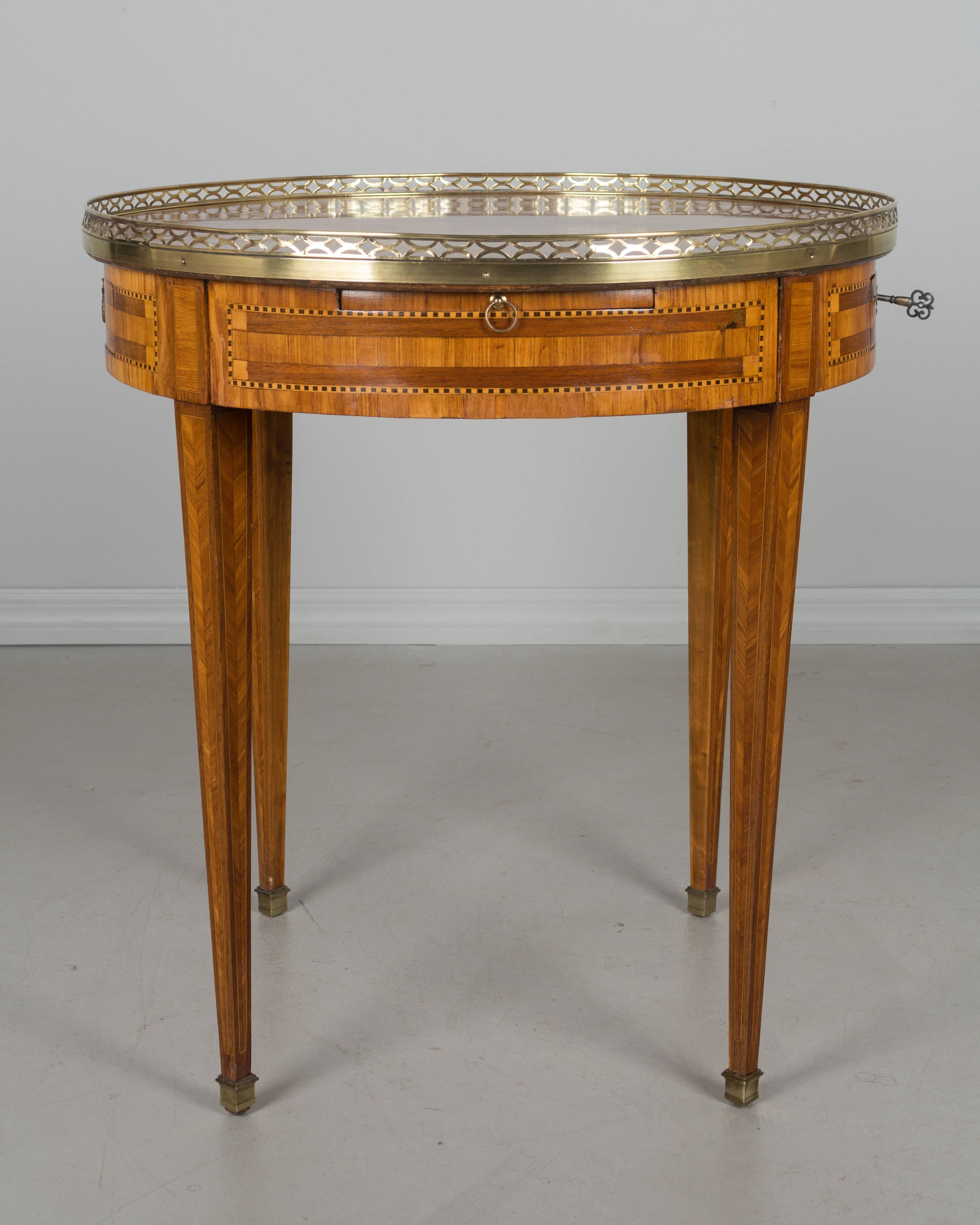 French Louis XVI style bouillotte table made of veneers of rosewood, tulipwood and mahogany. Two dovetailed drawers and two pull-out shelves with leather surface. Fine marquetry inlay of musical instruments on the top surrounded by a polished brass