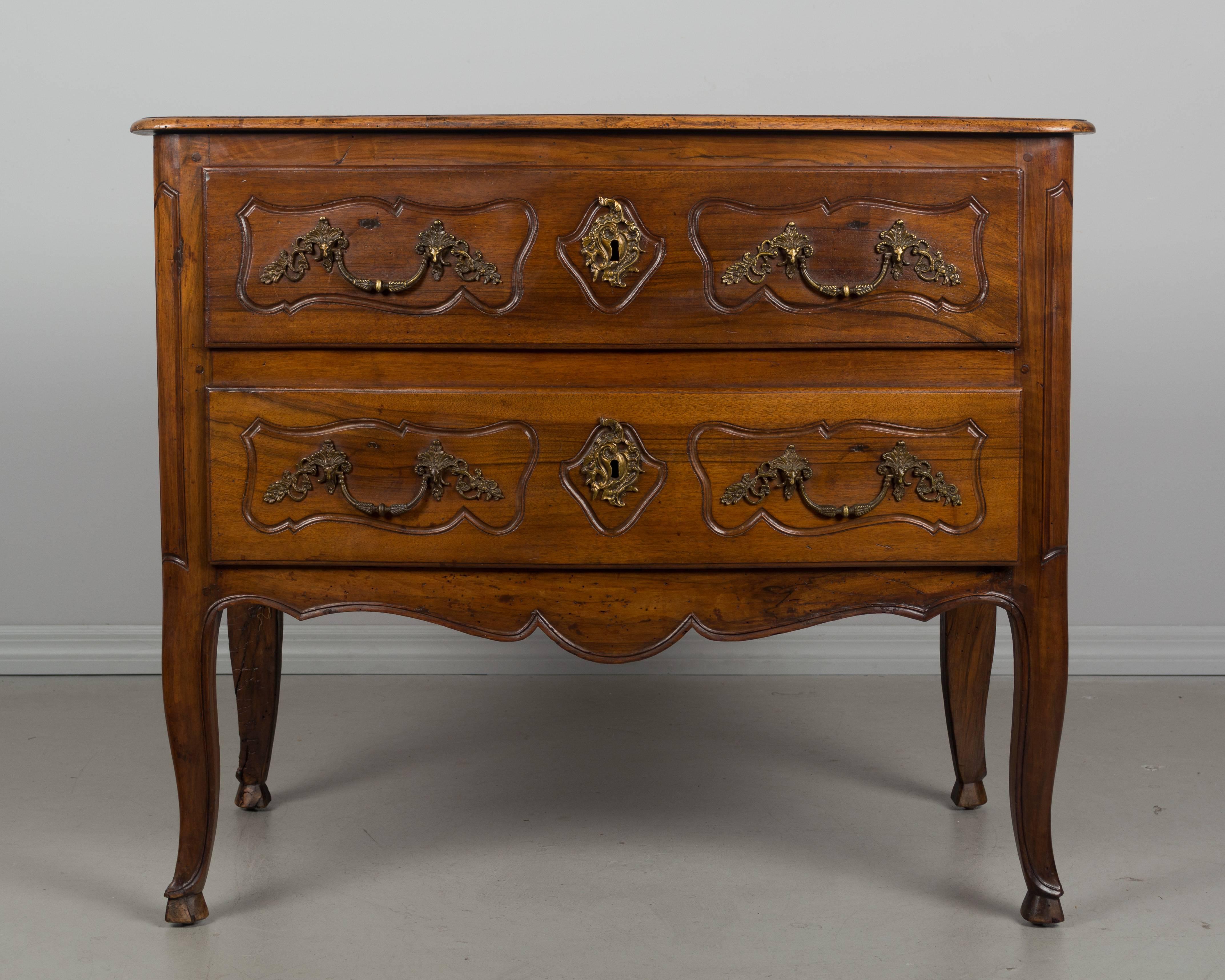 A 19th century Louis XV style commode from the South of France made of solid walnut with pegged construction and waxed finish. Two dovetailed drawers with brass hardware that is of the same period, but not original to the piece. Locks are present,