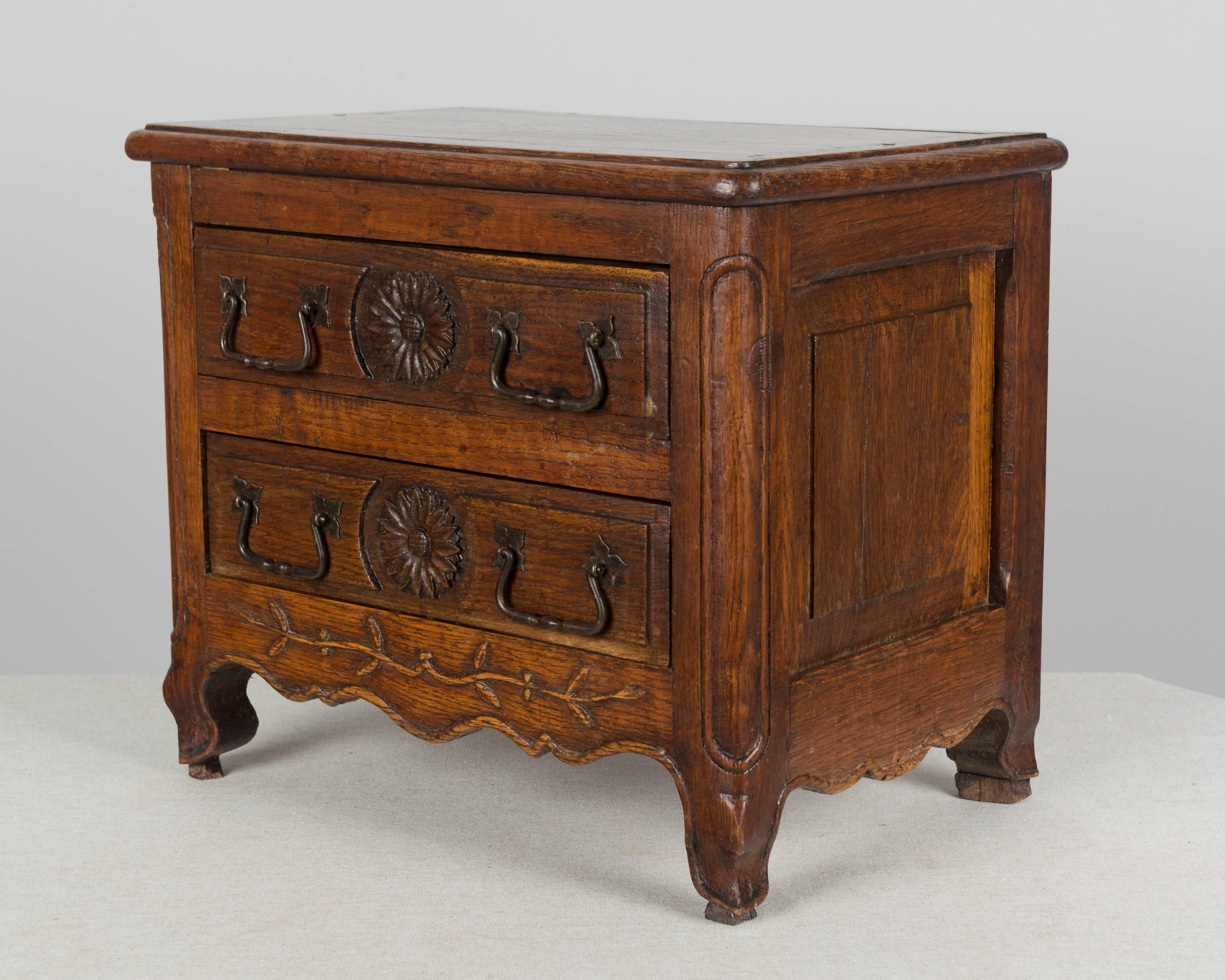 19th century Louis XV style Country French miniature commode made of solid oak. Simple hand-carved decoration of sunflowers on the drawers and a vine on the apron. Original hardware. Waxed patina. A good small chest, heavy for its size, with nice