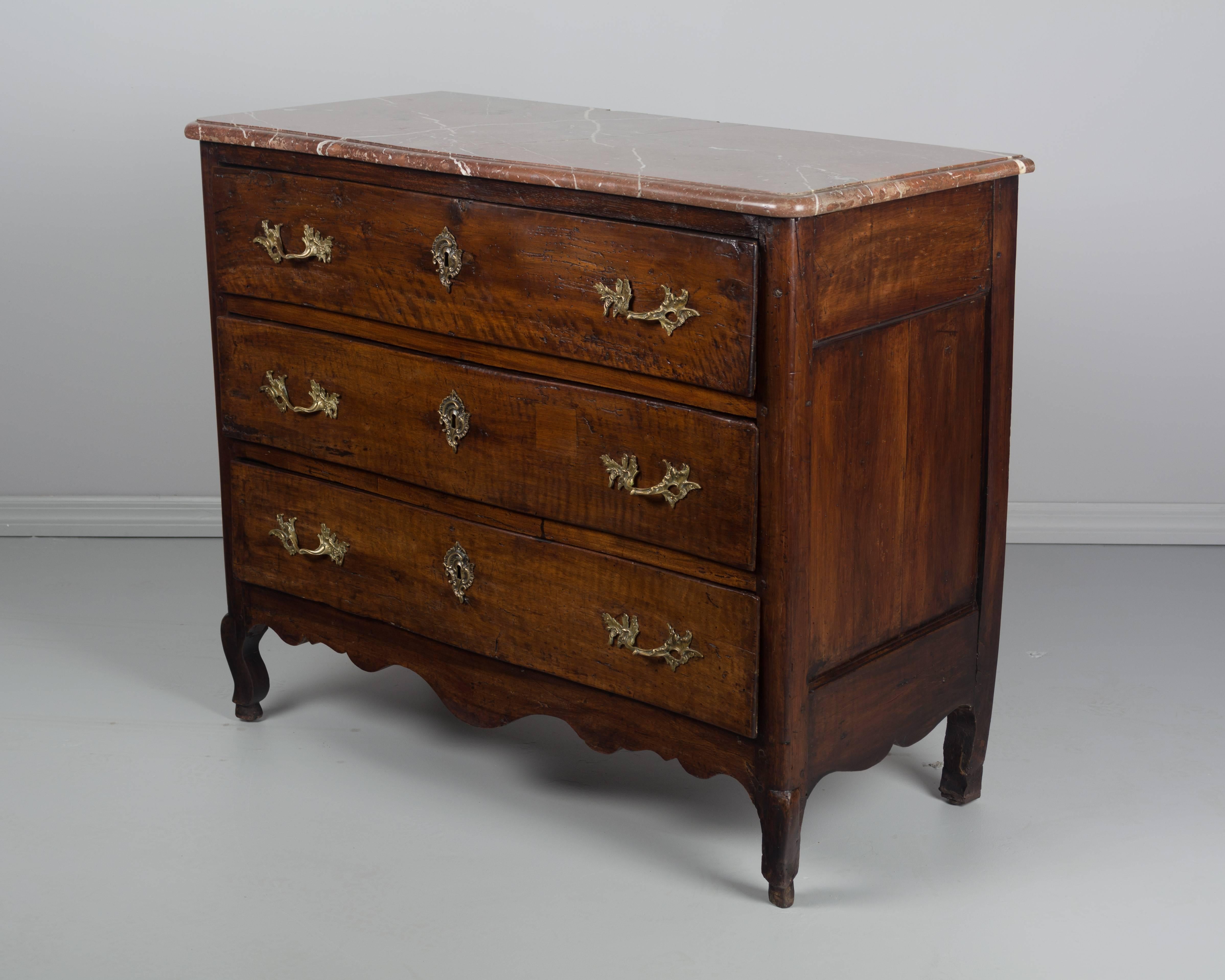 An 18th century Louis XV style Country French commode made of solid walnut with three dovetailed drawers. Original marble top has been repaired, as have the drawers and feet. Brass hardware is not original to the piece, but is of the same style and