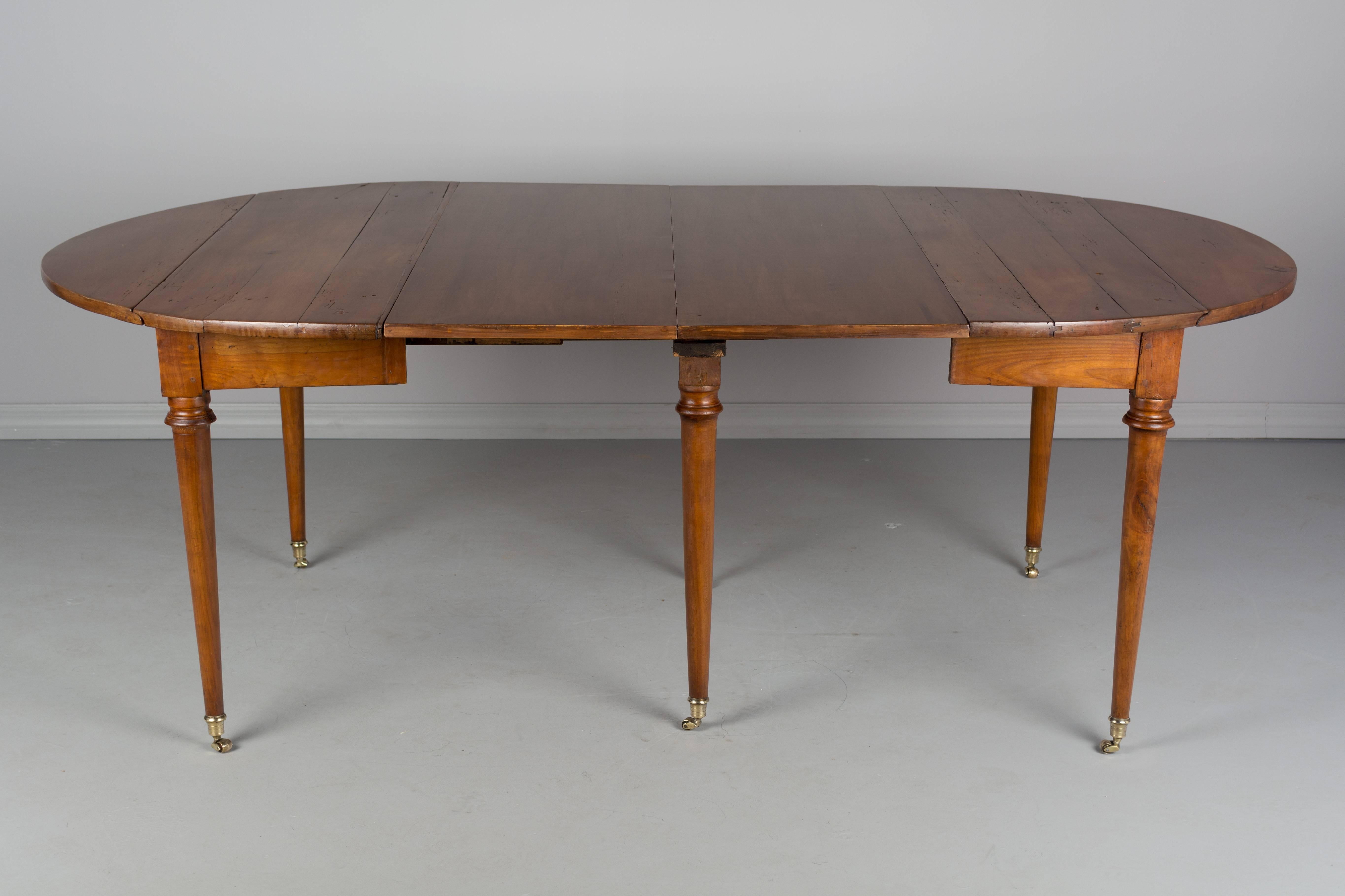 A 19th century French Louis XVI style drop-leaf dining table made of solid cherry. Six simple turned legs ending in polished cast brass wheels. Two 16 inch newer leaves are veneer of cherry, circa 1840-1860. 
Closed: 49