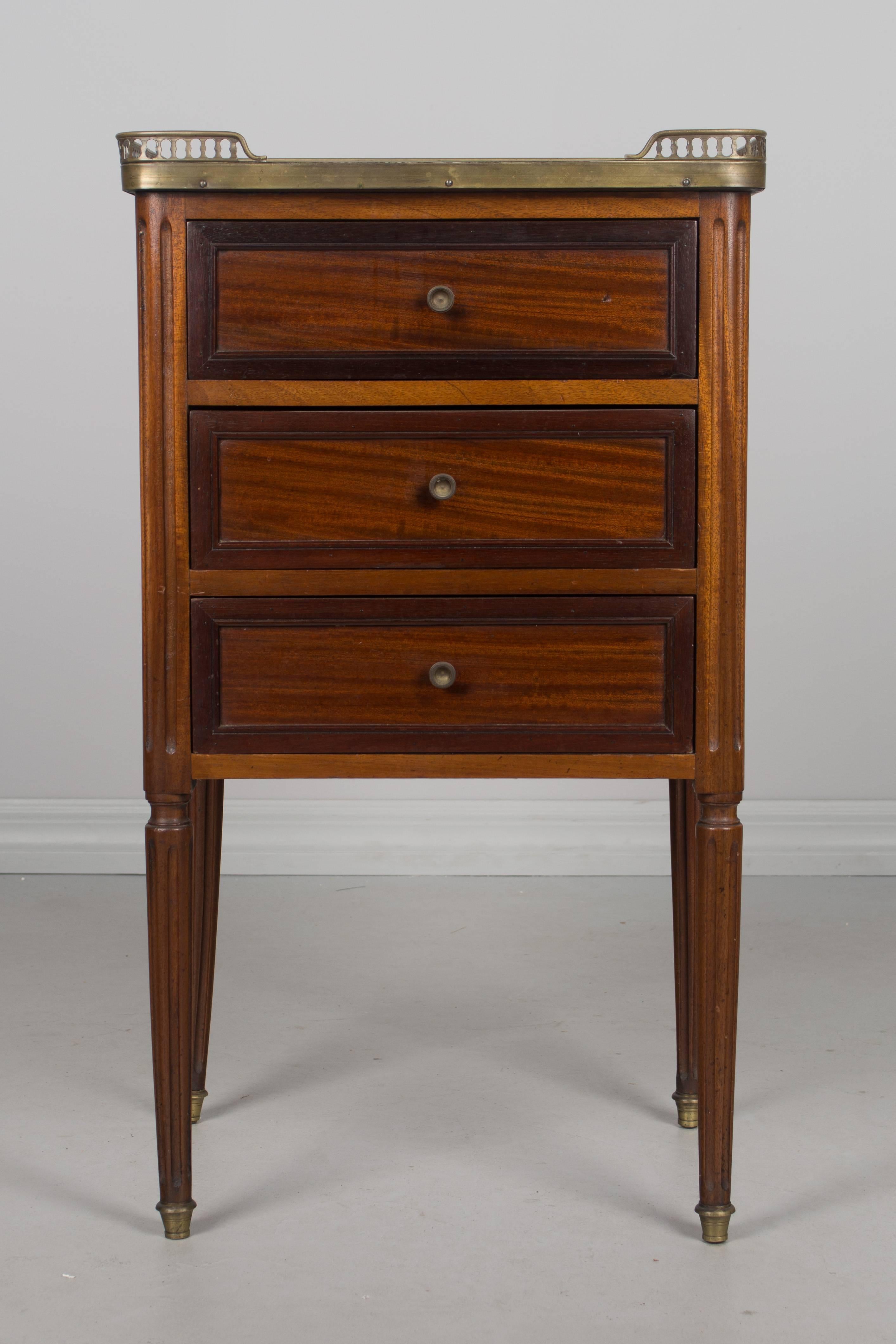 An early 20th century French Louis XVI style side table or nightstand made of solid mahogany with three dovetailed drawers and a white marble top surrounded by a brass gallery. Note the back left leg is a little bent, not broken. More photos