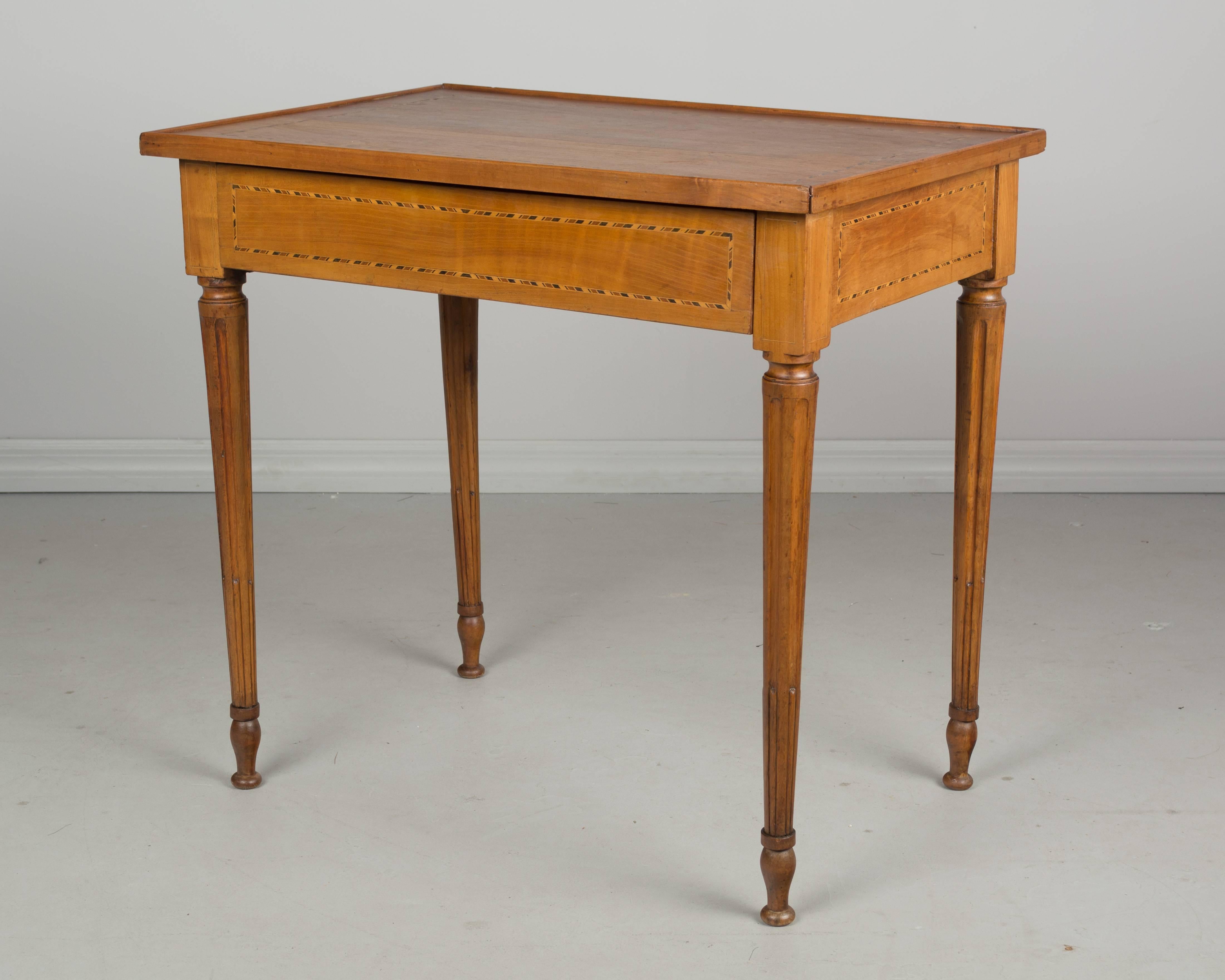 A 19th century French Louis XVI style side table made of cherrywood with inlay detail, fluted legs and a single drawer. Restoration on the bottom of the legs. More photos available upon request. We have a large selection of French antiques at