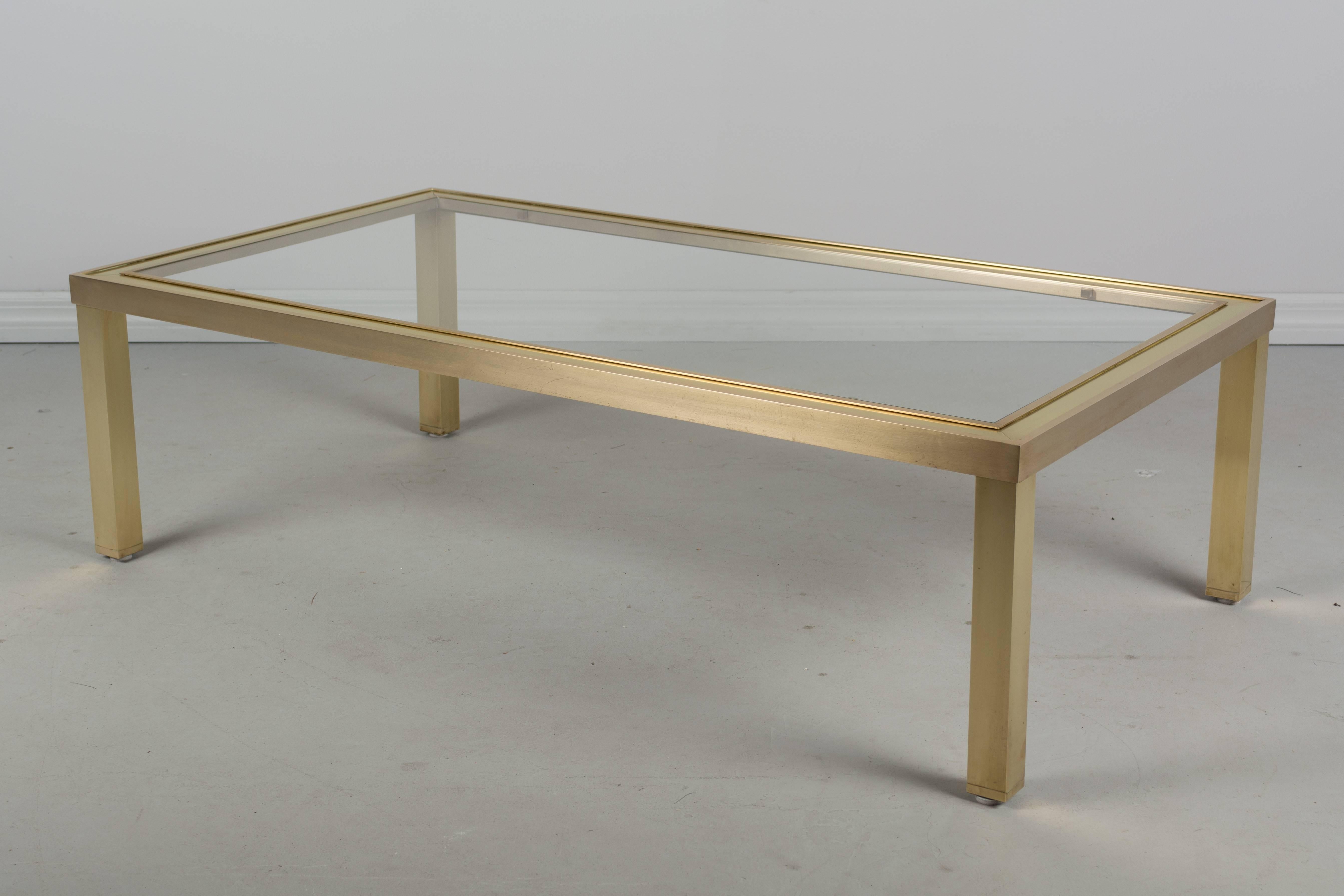 A Mid-Century Modern Maison Jansen style glass top coffee table with base of brushed nickel and polished brass. 
 
 