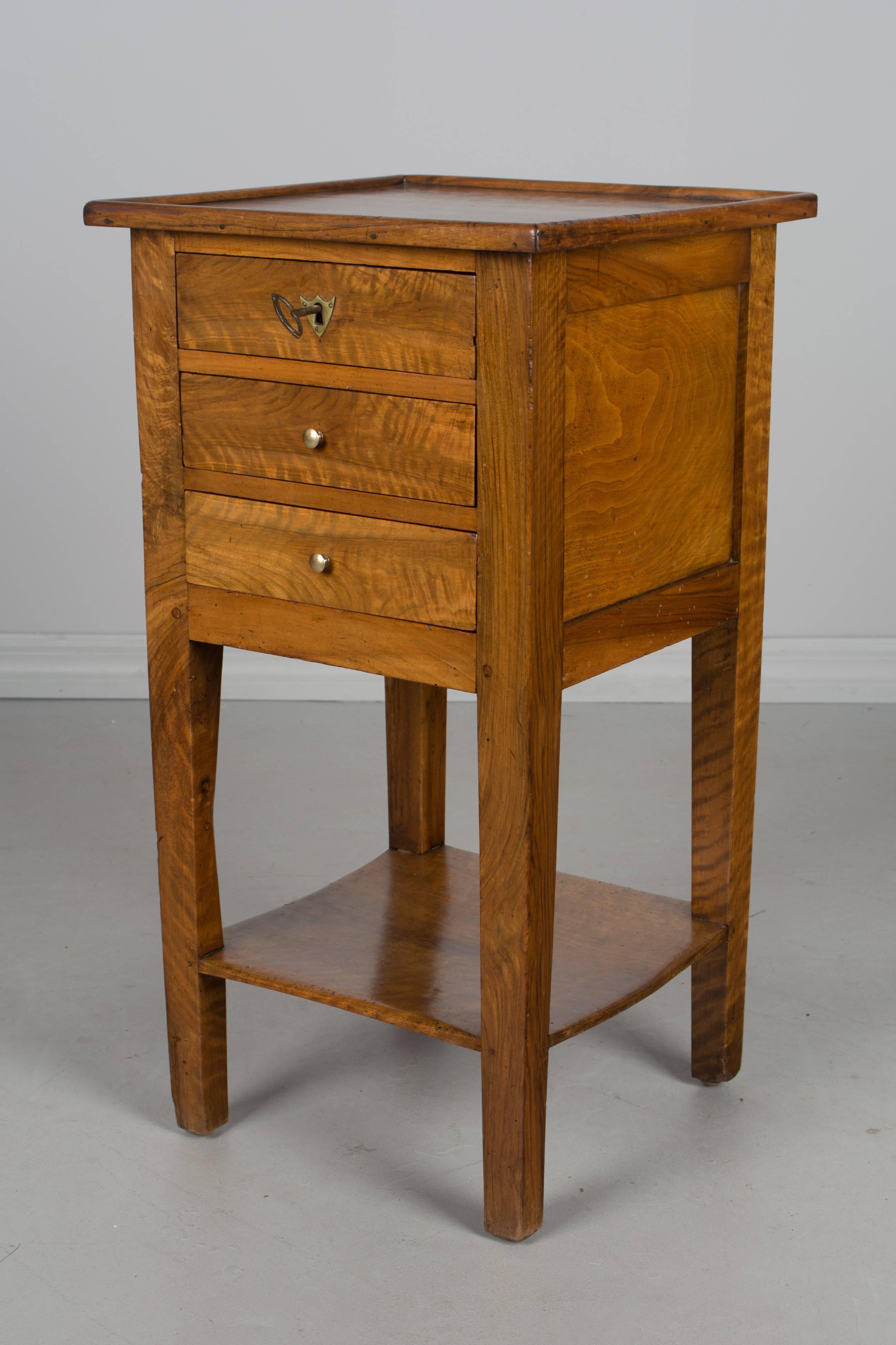 A Country French side table made of solid walnut and finished on all four sides. Beautiful wood grain with large knot on the back. Waxed finish. Three dovetailed drawers with working lock and key. (Key is not original) 
More photos available upon