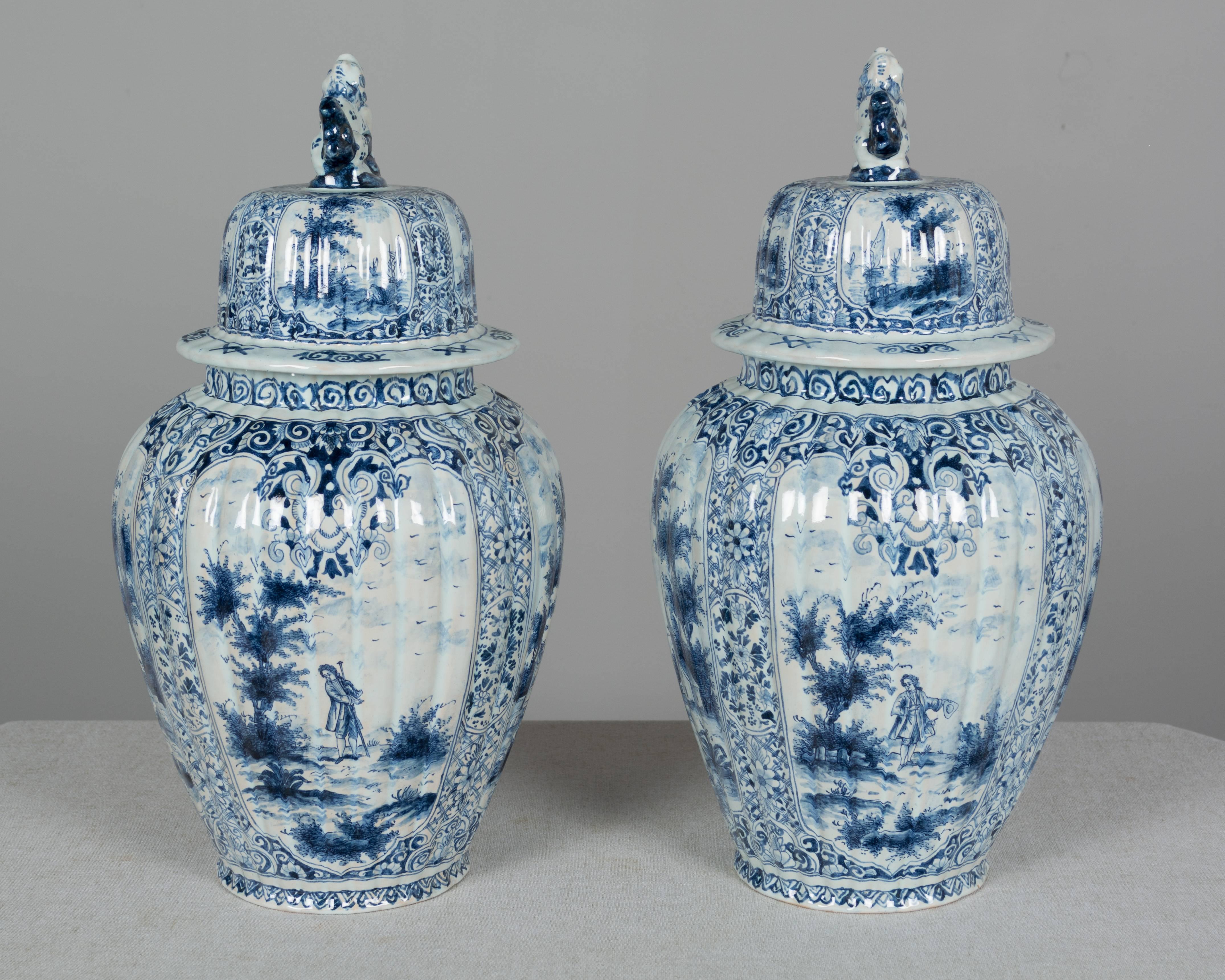 A pair of Delft faience blue and white ginger jars with traditional ribbed urn form and lids topped with foo lion knobs. Each with four painted panels bordered with elaborate floral decoration and depicting coastal scenes with boats and figures in