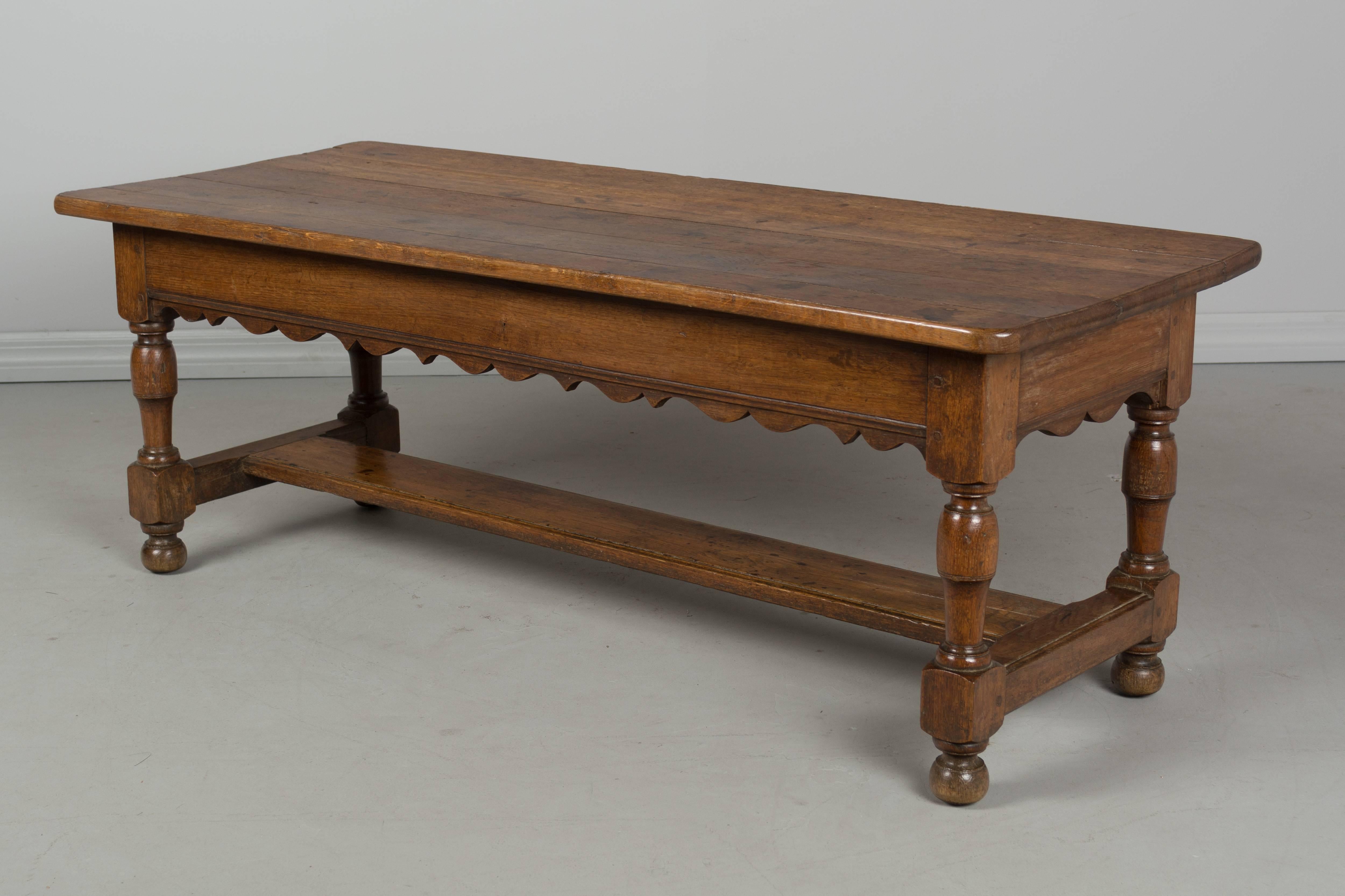 A 19th century Country French bench made of solid oak with scalloped apron and turned legs. Very sturdy with pegged construction and stretcher. Nice proportions for use as a coffee table. Waxed finish. Top is slightly off center. More photos
