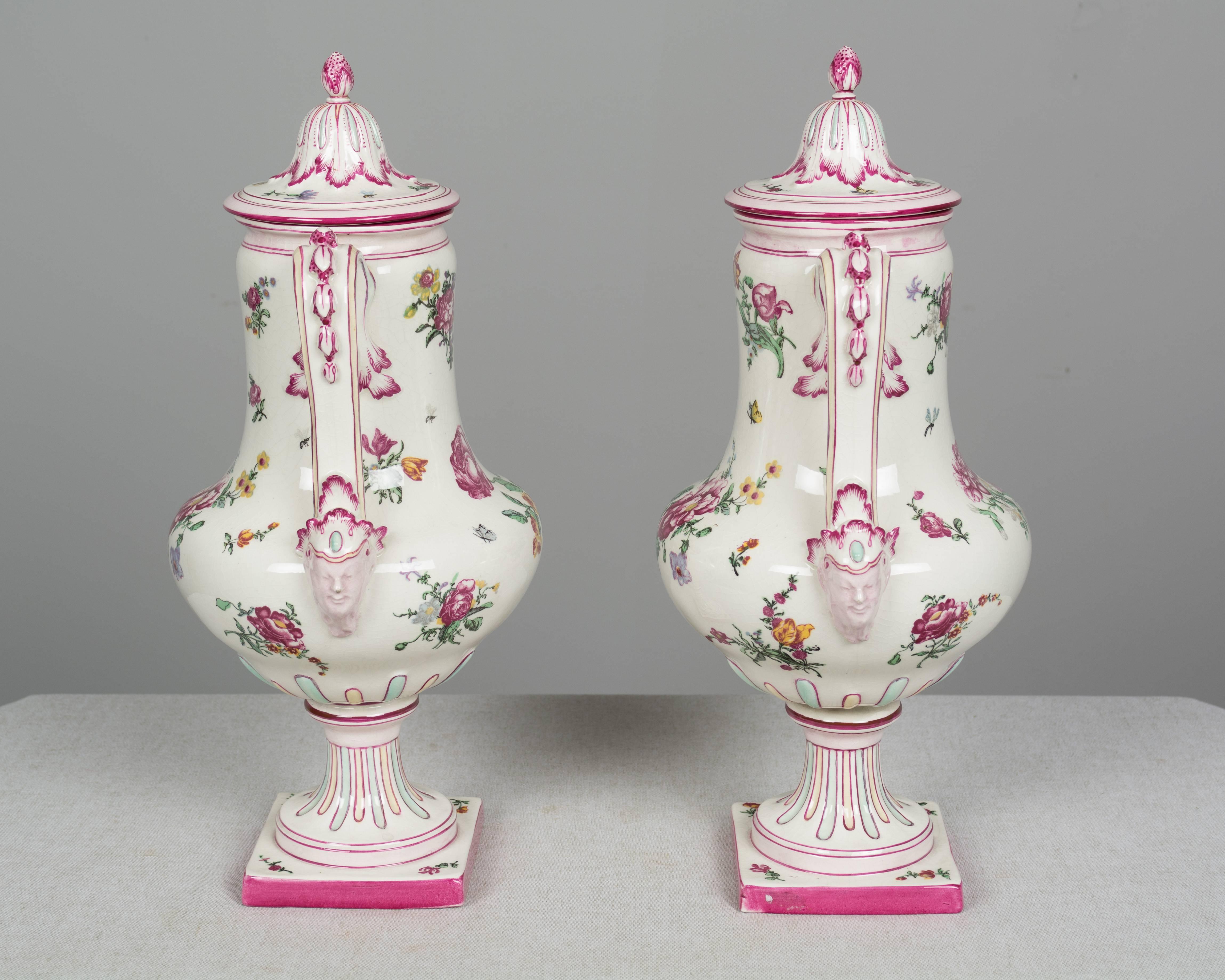 A pair of 19th century French Gien faience urns with hand-painted floral decoration. Nice form with double handles and square pedestal base. Lids with strawberry knobs. Gien stamp on underside, circa 1866. Measures: 16.5" H x 9" W x