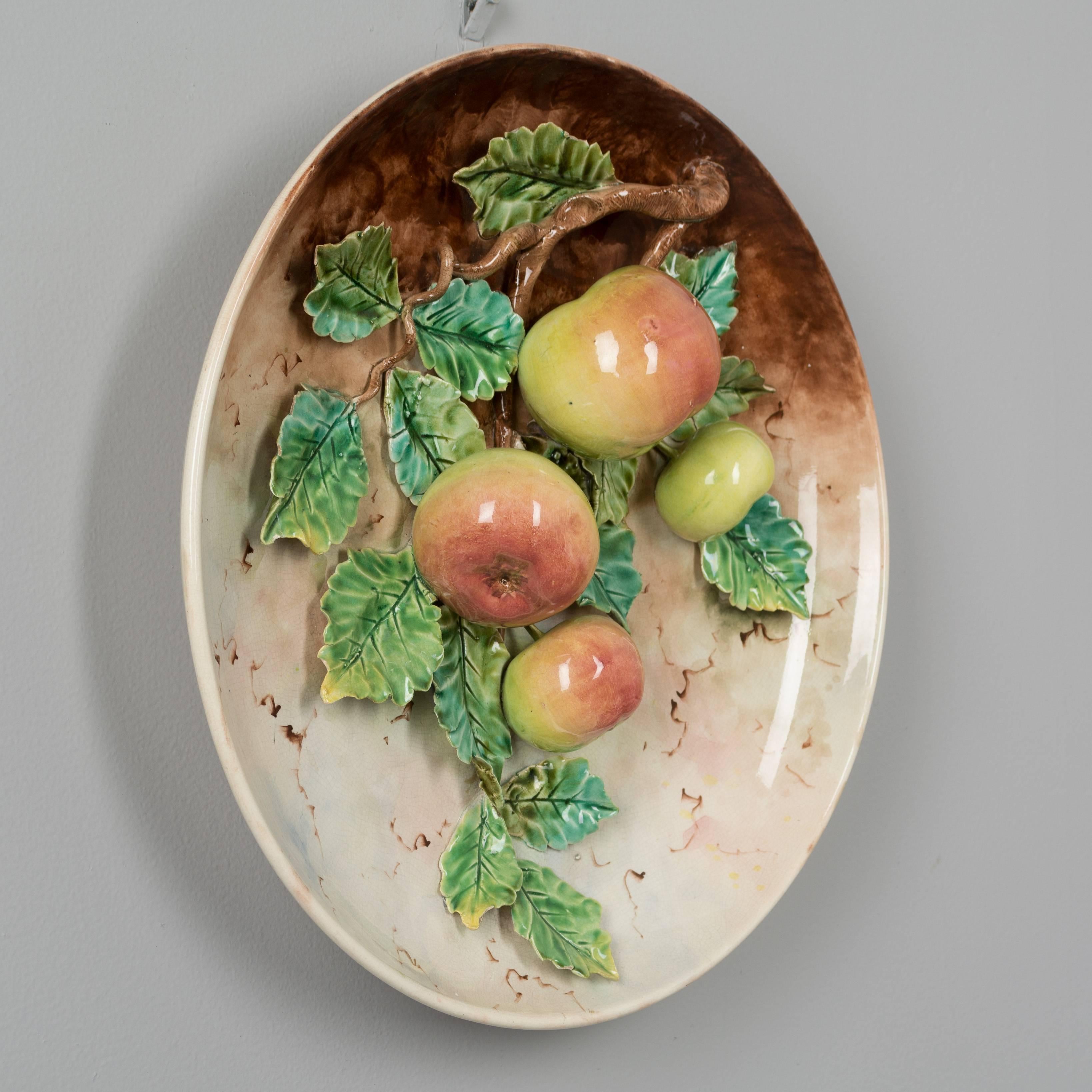A large 19th century French Barbotine Majolica platter with four red and yellow apples hanging from a tree branch covered with green leaves. Sculpted in high relief and hand-painted with vivid color. Good condition with minor loss on one leaf. We