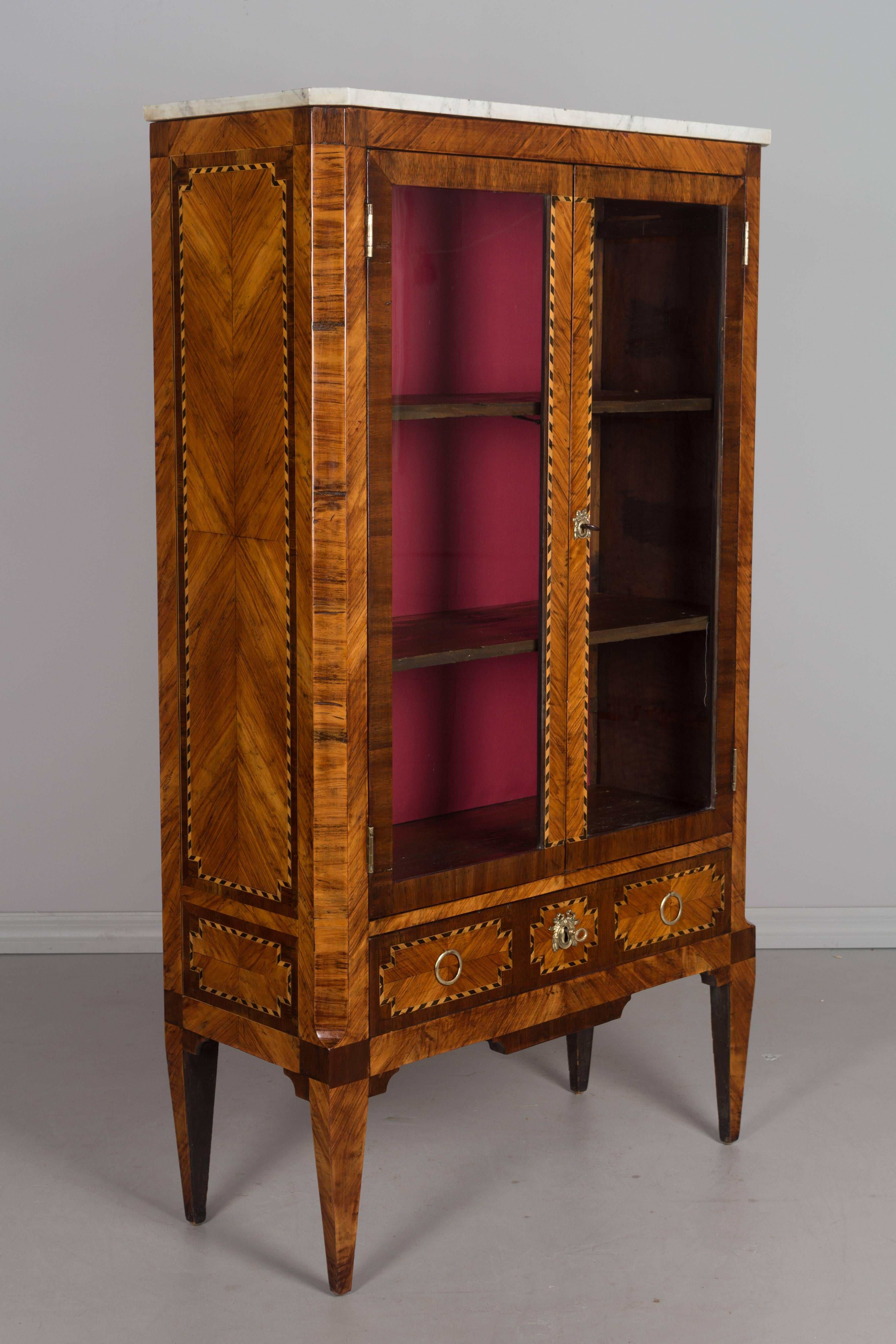 A fine 18th century French Louis XVI marquetry bibliotheque, or bookcase with inlaid veneer of rosewood, walnut and mahogany. Dovetailed drawer below glass paned doors opening to three shelves with newly lined fabric interior. Bronze hardware and