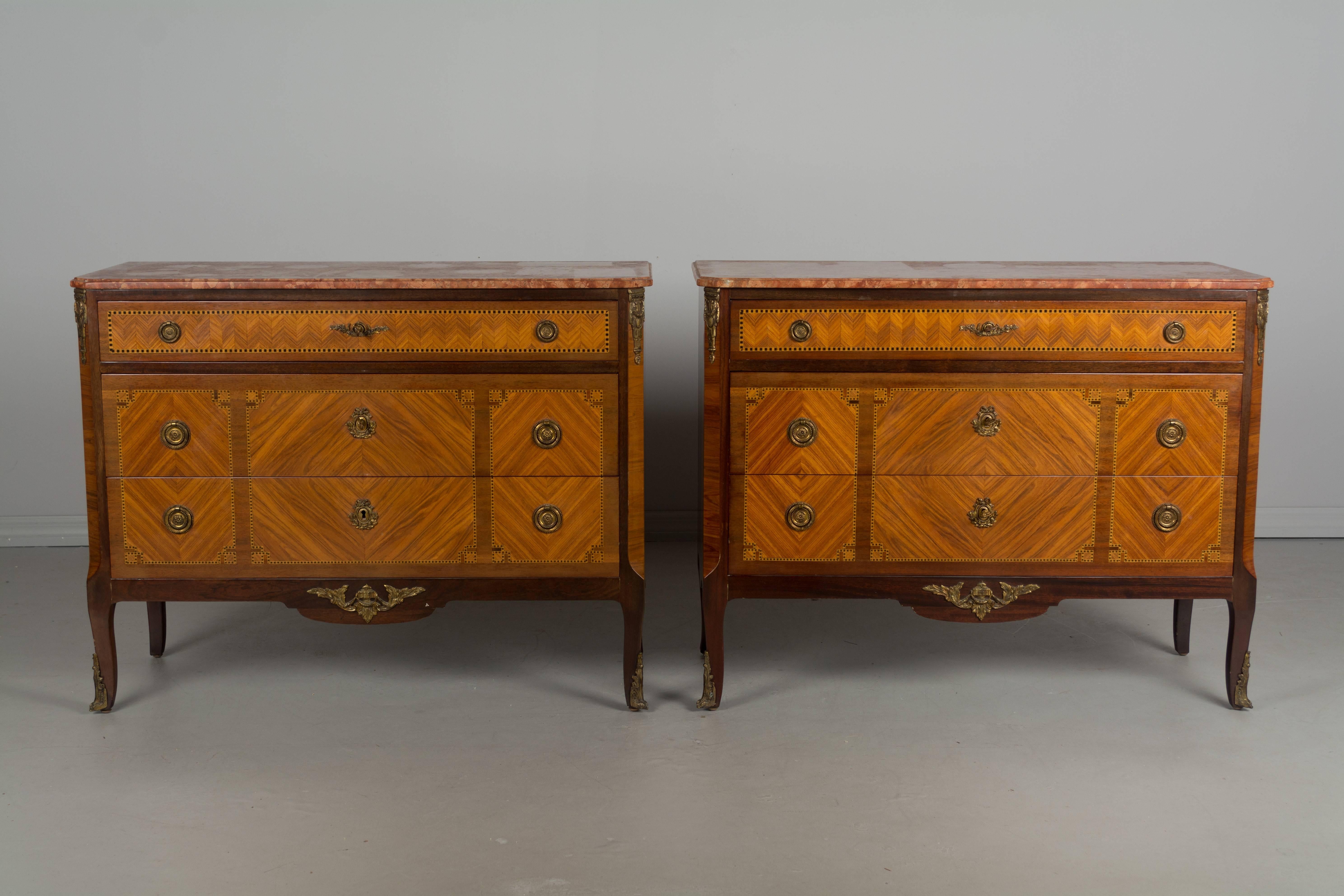 Pair of French Louis XVI style marquetry commodes or bachelor's chests, made of mahogany and inlaid with various exotic wood veneers. Three dovetailed drawers with brass hardware, working locks and keys (one key is missing from one of the commodes).