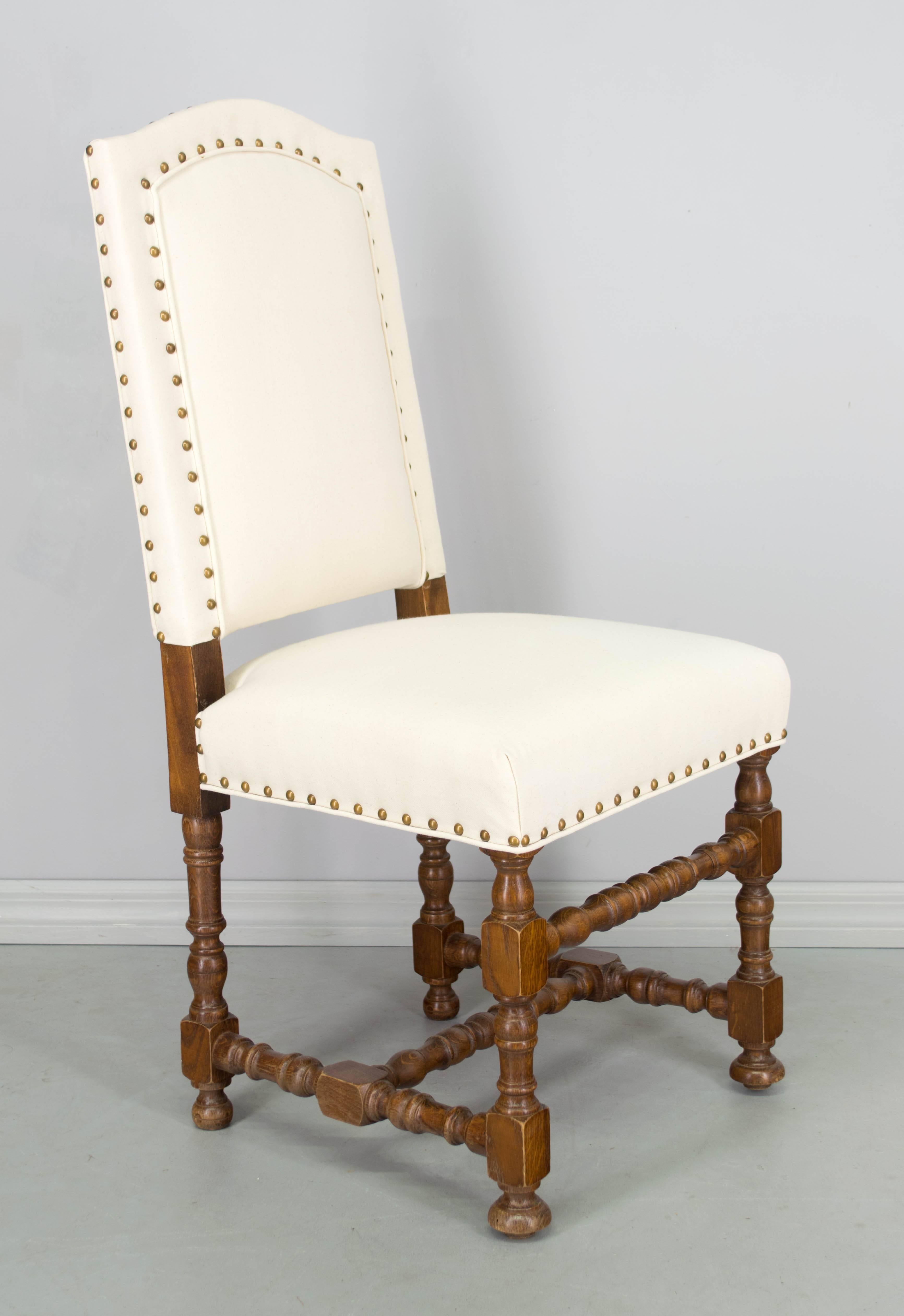 Set of six French Louis XIII style dining chairs made of oak with nicely turned wood legs and stretcher. Newly reupholstered in natural canvas with brass nailhead trim. Sturdy and comfortable seating. We have a large selection of French antiques.