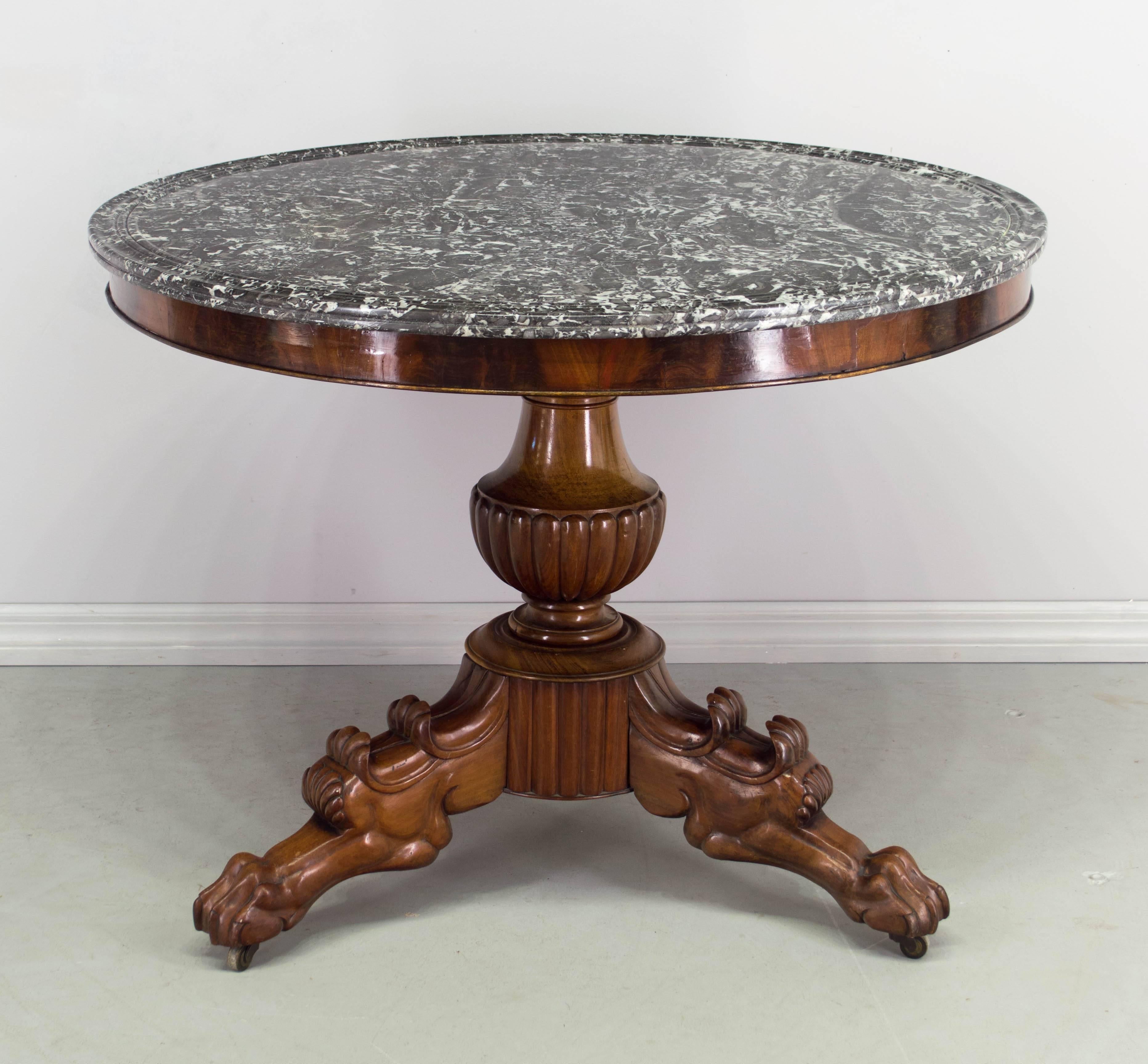19th century French Napoleon III gueridon or center table with carved mahogany pedestal base having a fluted urn shaped column and three stylized lion legs. A Classic form with exception hand carving. Original Saint Anne double grooved marble top