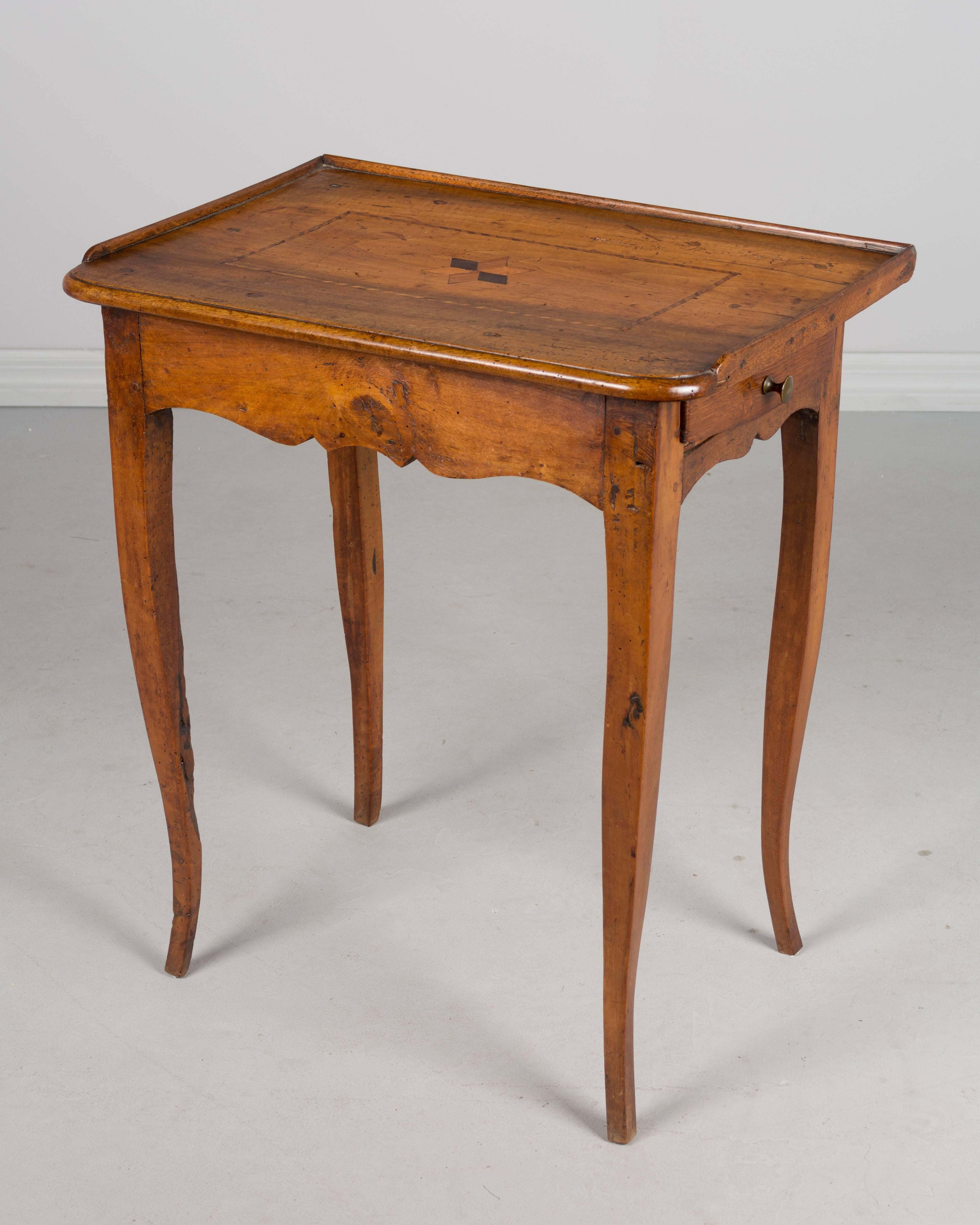 18th century period Louis XV writing or side table made of walnut and oak. Single drawer on right side. Top has simple star inlaid design and curved front corners with wood trim on three sides. Slim curved legs. All original. Waxed patina. The face