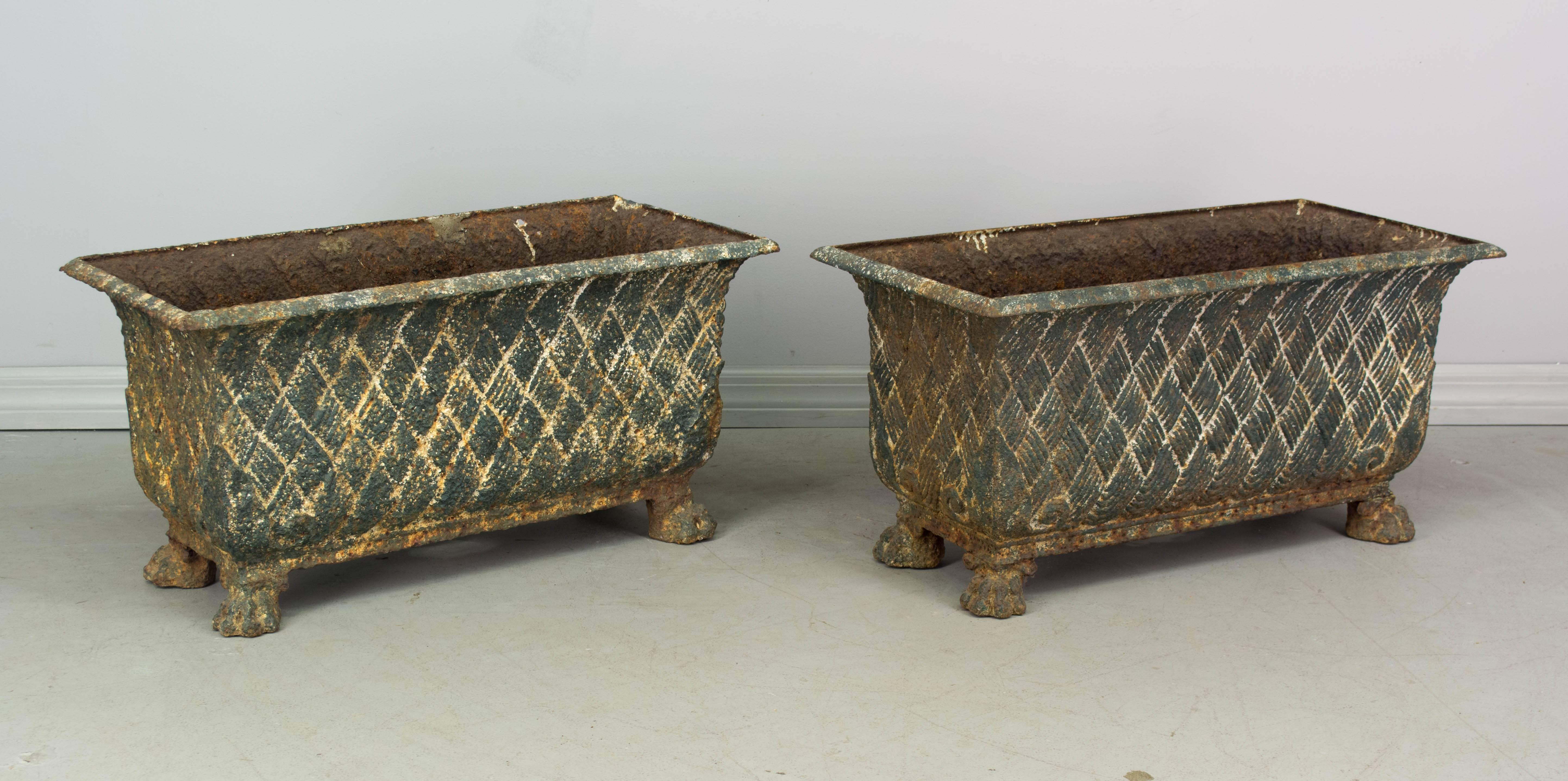 Pair of 19th century French cast iron planters with old green painted patina. Oblong shape with a basketweave pattern and lion paw feet. We have a large selection of French antiques. Please visit our web site.