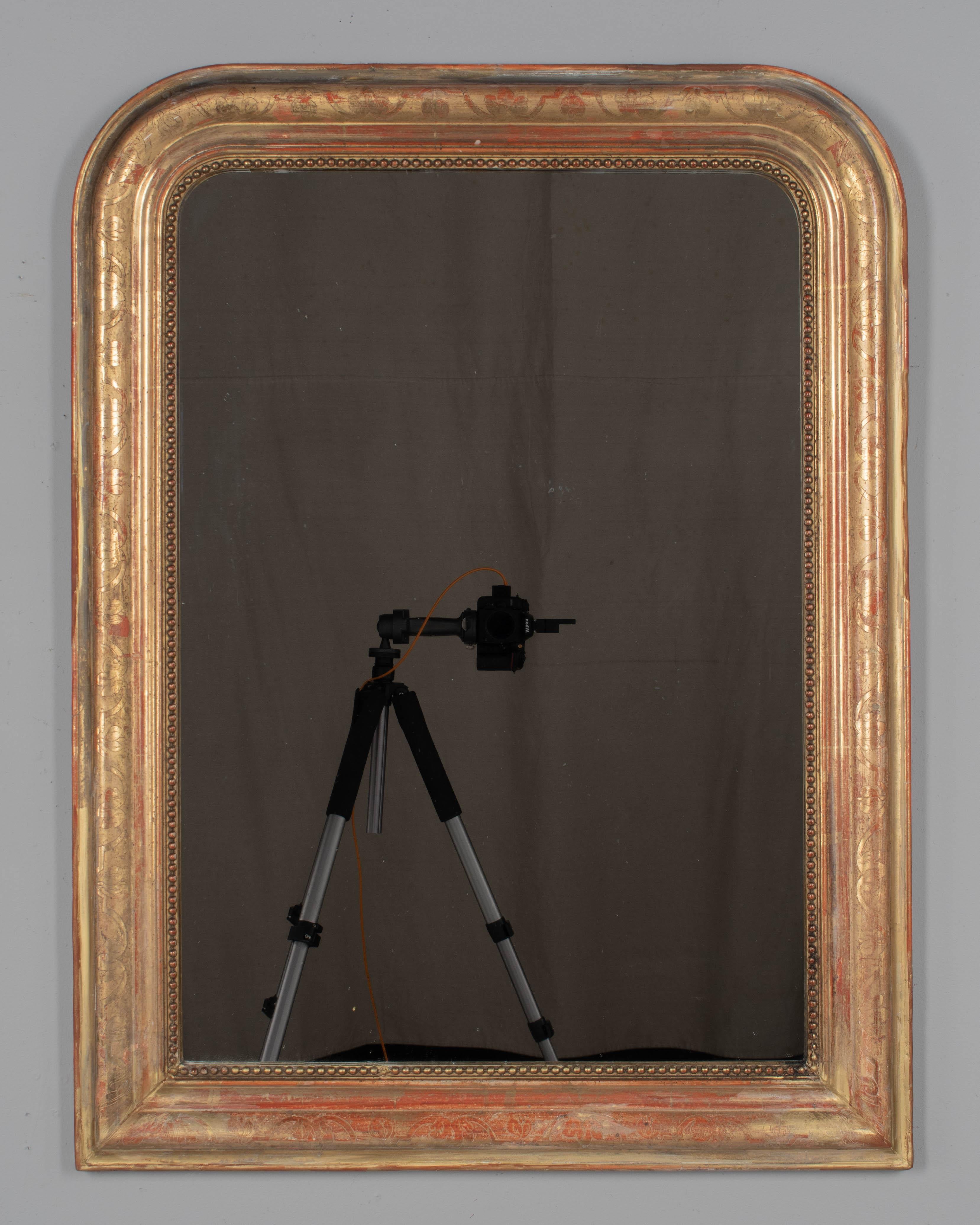 Miroir en bois doré de style Louis Philippe, datant de la fin du XIXe siècle, avec un décor floral incisé, des angles supérieurs incurvés et une bordure intérieure en perles. Belle patine d'usage avec sous-couche rouge et finition dorée chaude.