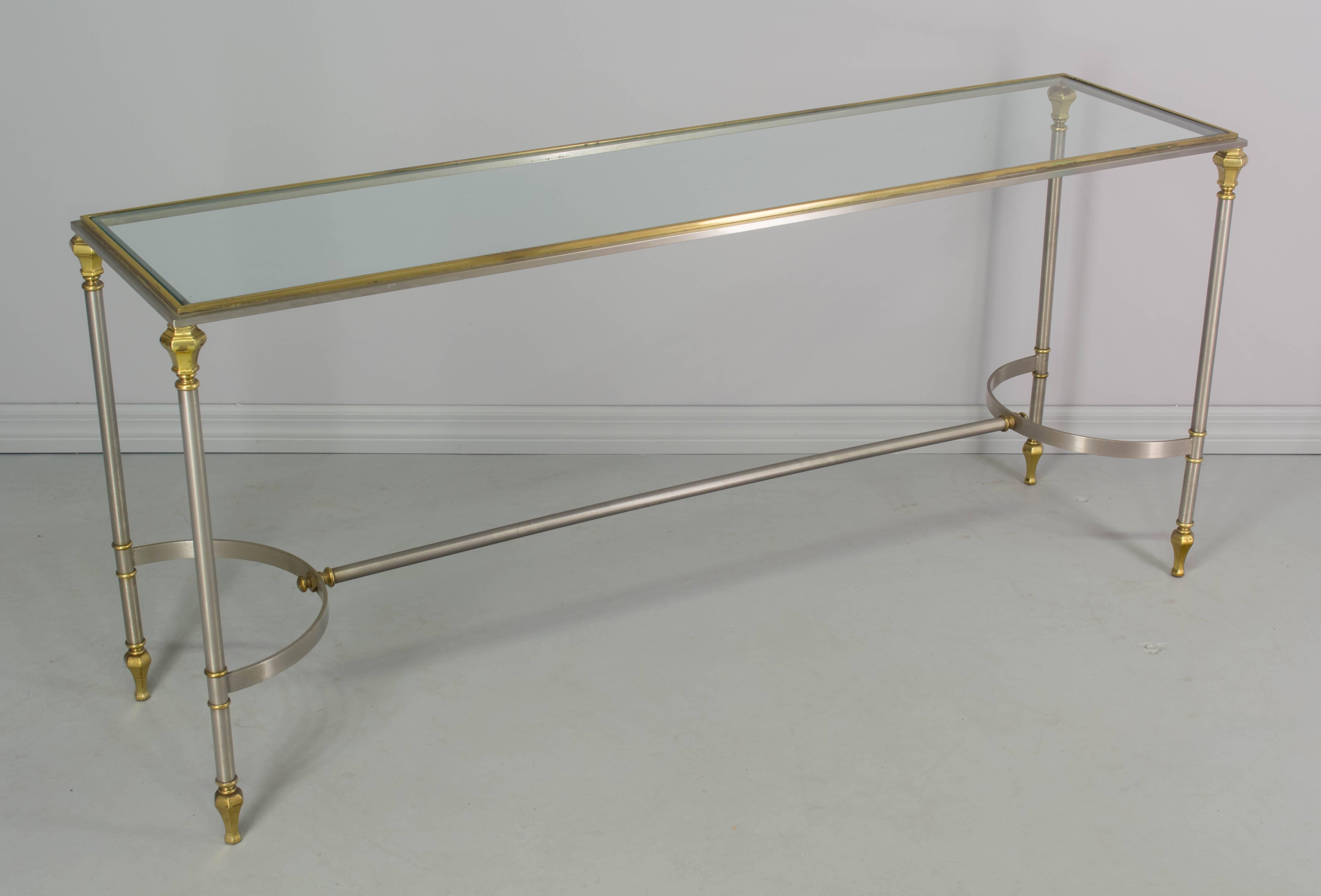 An elegant Mid-Century Modern console or sofa table in the style of Maison Jansen. Brushed steel with brass accents and glass top. We have a large selection of French antiques. Please visit our web site.
 