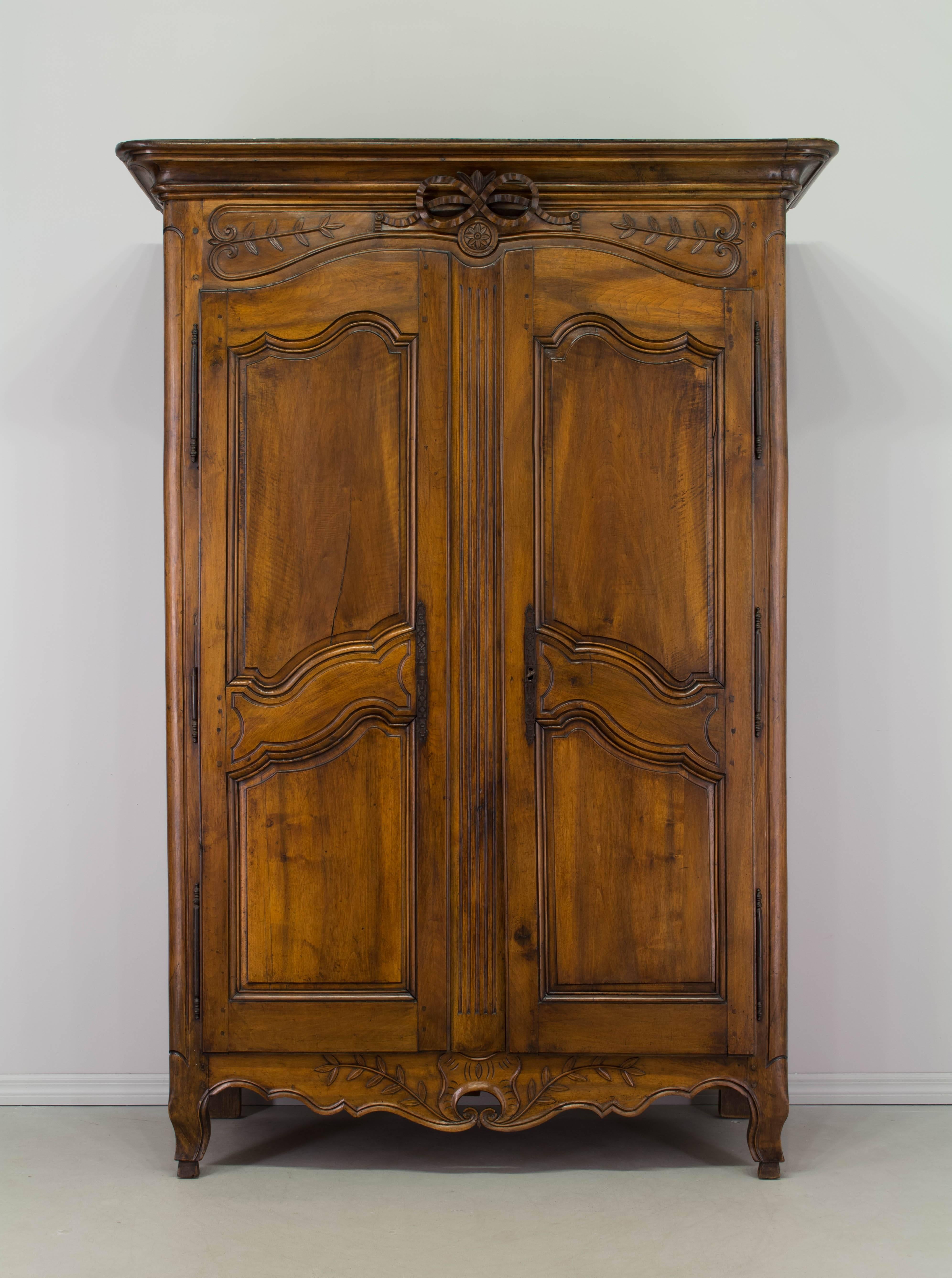 18th century French Louis XV bridal armoire for Provence made of sold walnut with raised panel doors, a pierced apron and a carved wedding ribbon below a molded crown. Three raised panels on the sides, mortise and tenon joints and pegged