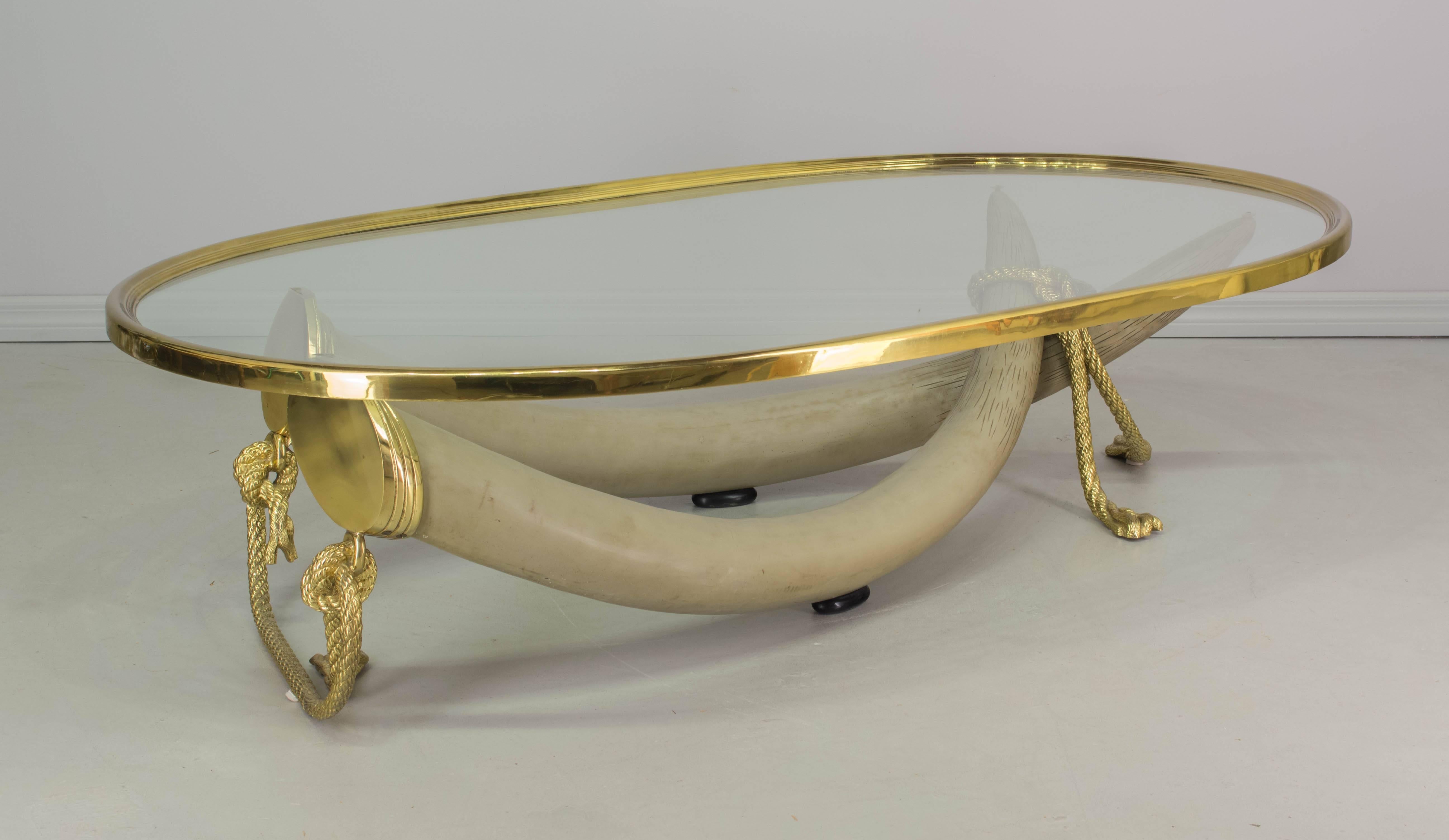 A large Spanish coffee table of exceptional quality designed by Valenti of Madrid. Sculptural base is comprised of two life-size resin faux elephant tusks capped and "tied" together with solid polished brass ropes. Heavy brass banded glass