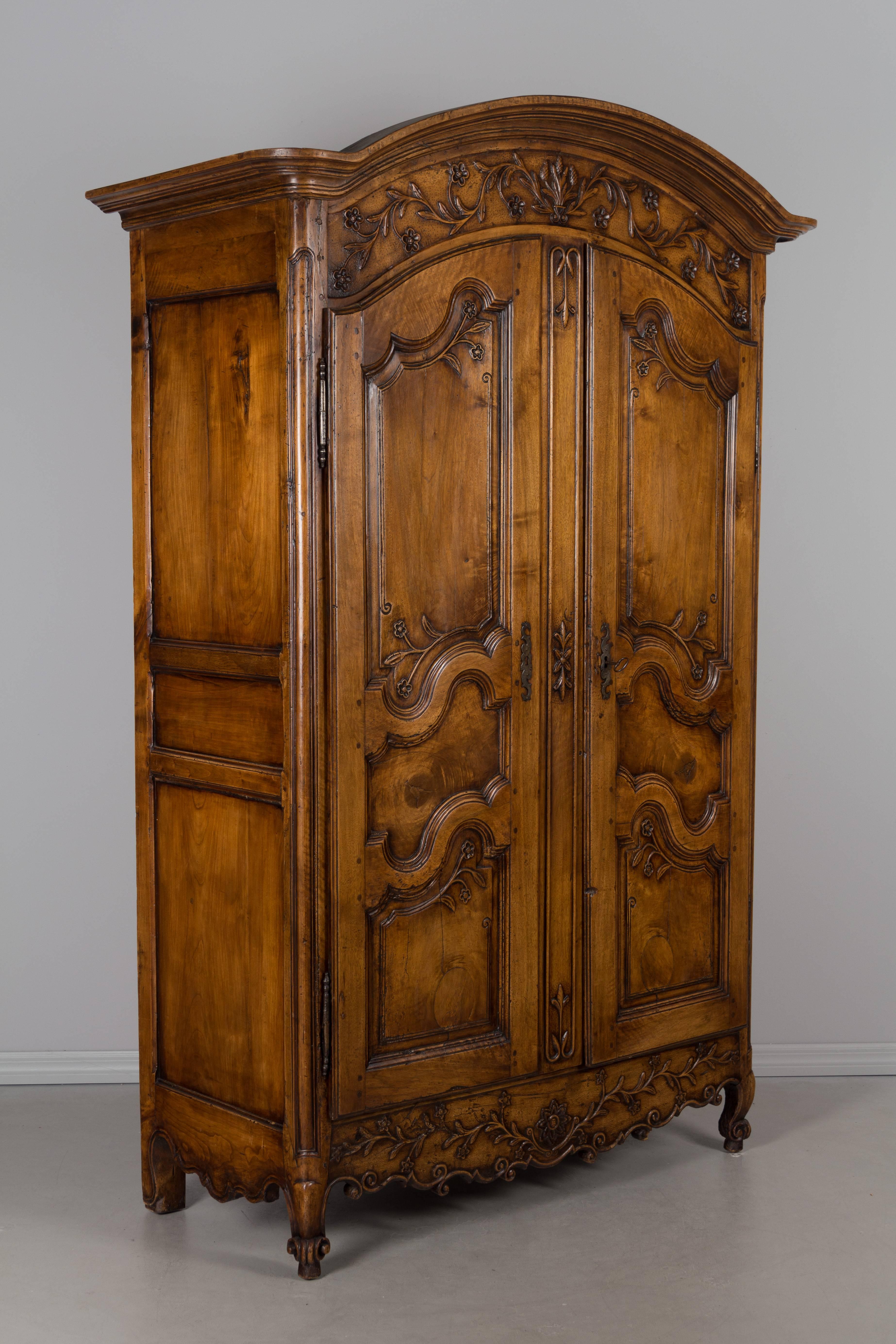 An 18th century Louis XV country French armoire from Burgundy, made of solid walnut and cherry with a chapeau de gendarme crown. Beautiful patterned knots in the wood are nicely framed on the three panels of each door. Floral vines, hand-carved in