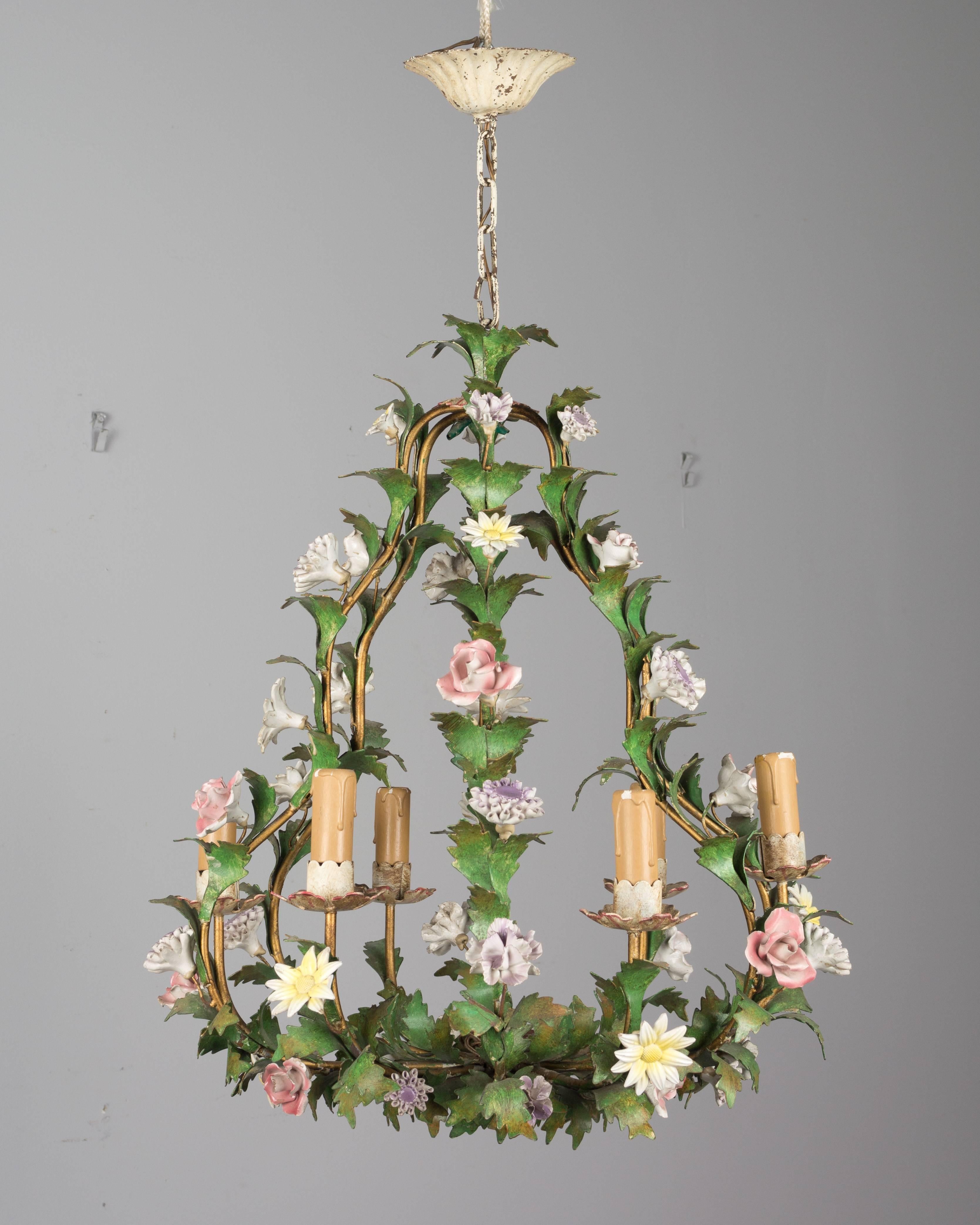 A charming Italian painted tole six-light chandelier with a variety of porcelain flowers including pink roses, yellow daisies and lavender mums, circa 1940-1950. In good condition with vivid color. Chips to some of the porcelain and a small welded