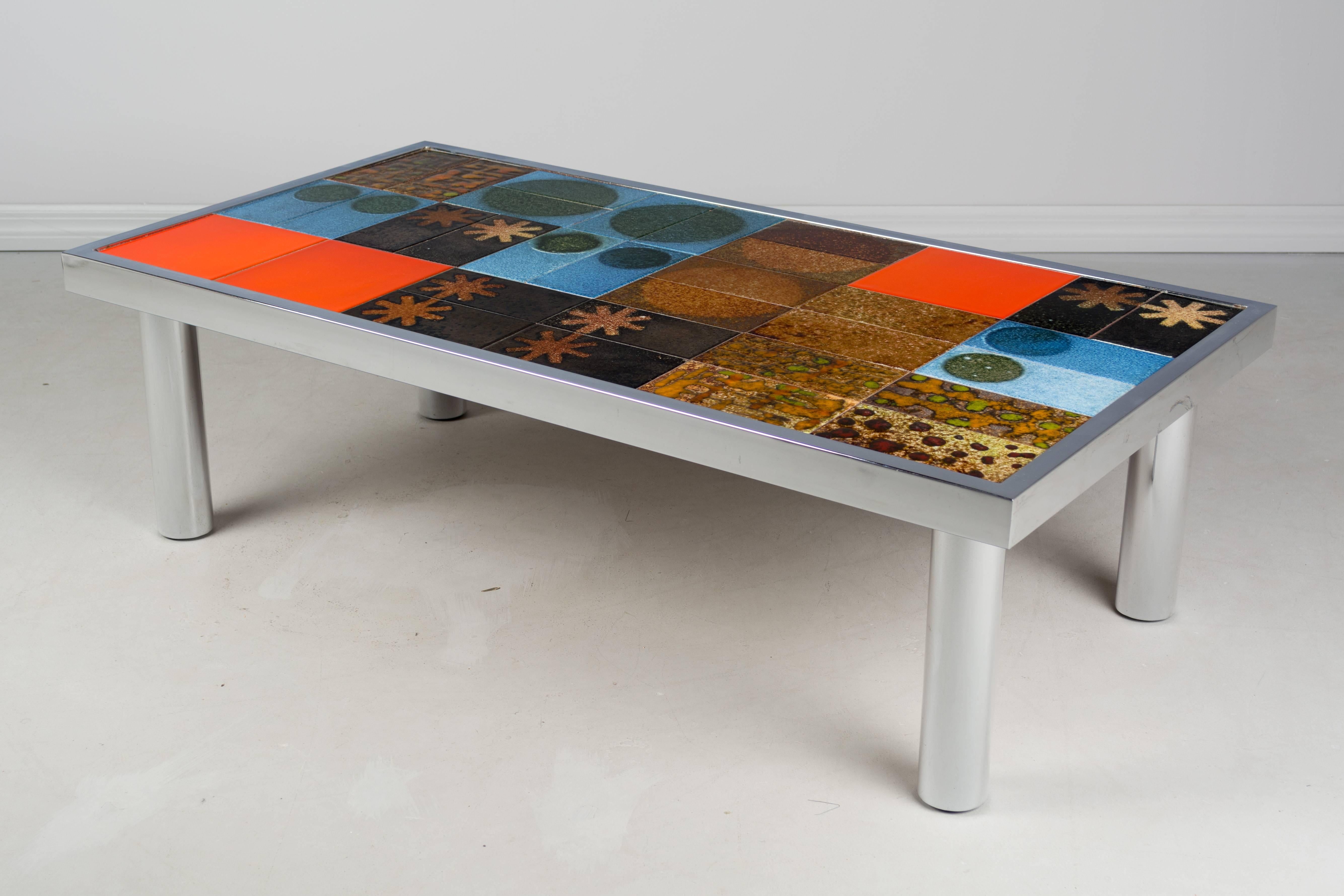 Mid-Century Modern Roger Capron style tile top coffee table with polished chrome base. Glazed ceramic tiles in vivid colors, artfully arranged in a random pattern. Heavy tubular legs with inset screws to adjust the height for the flooring surface.
