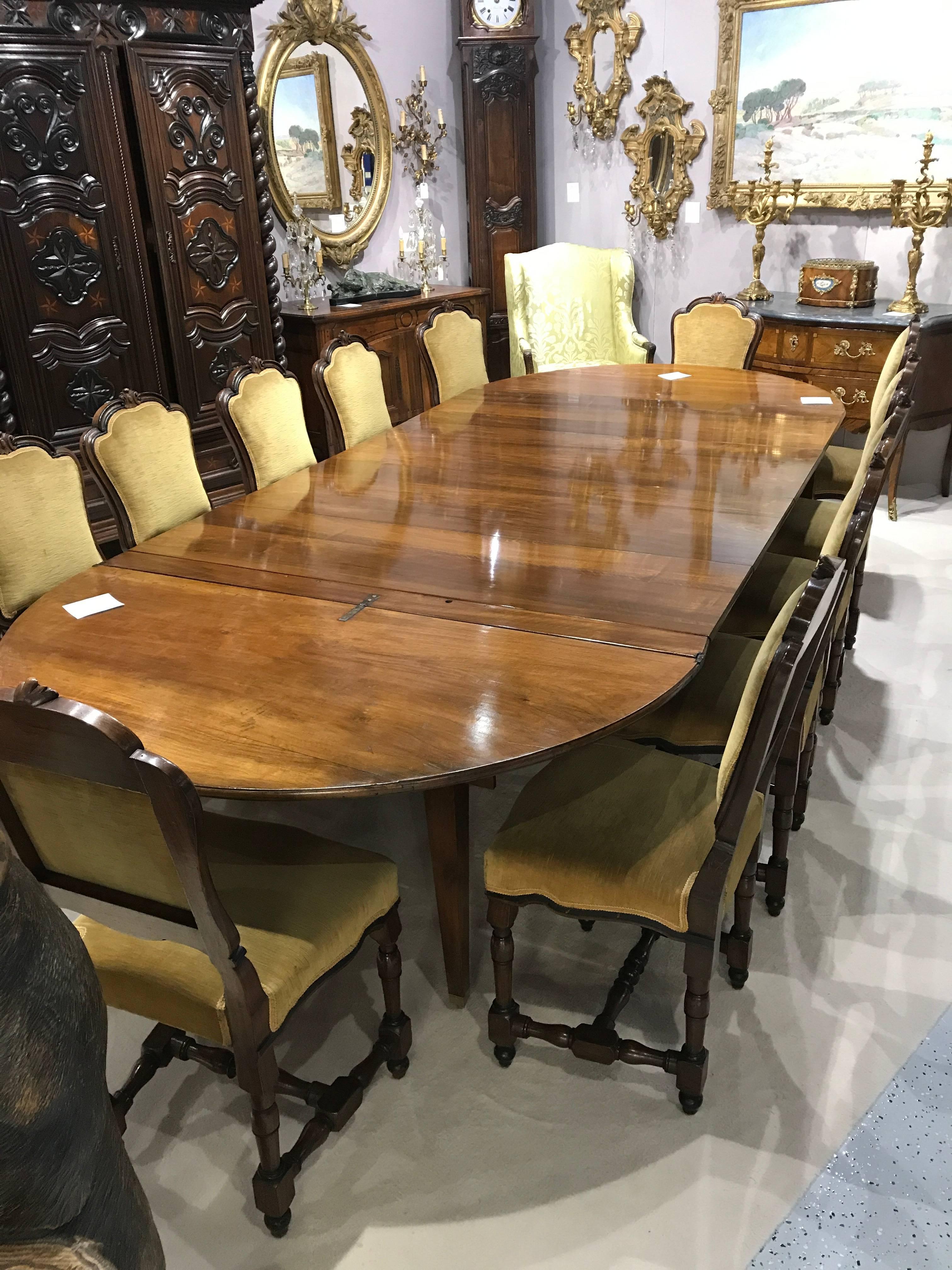 A large 19th century French Directoire walnut dining table with five new leaves that expands from a demi-lune to 13 feet long. When fully extended this table can seat 16-18 people. Very sturdy and well constructed with ten legs on brass castors. New