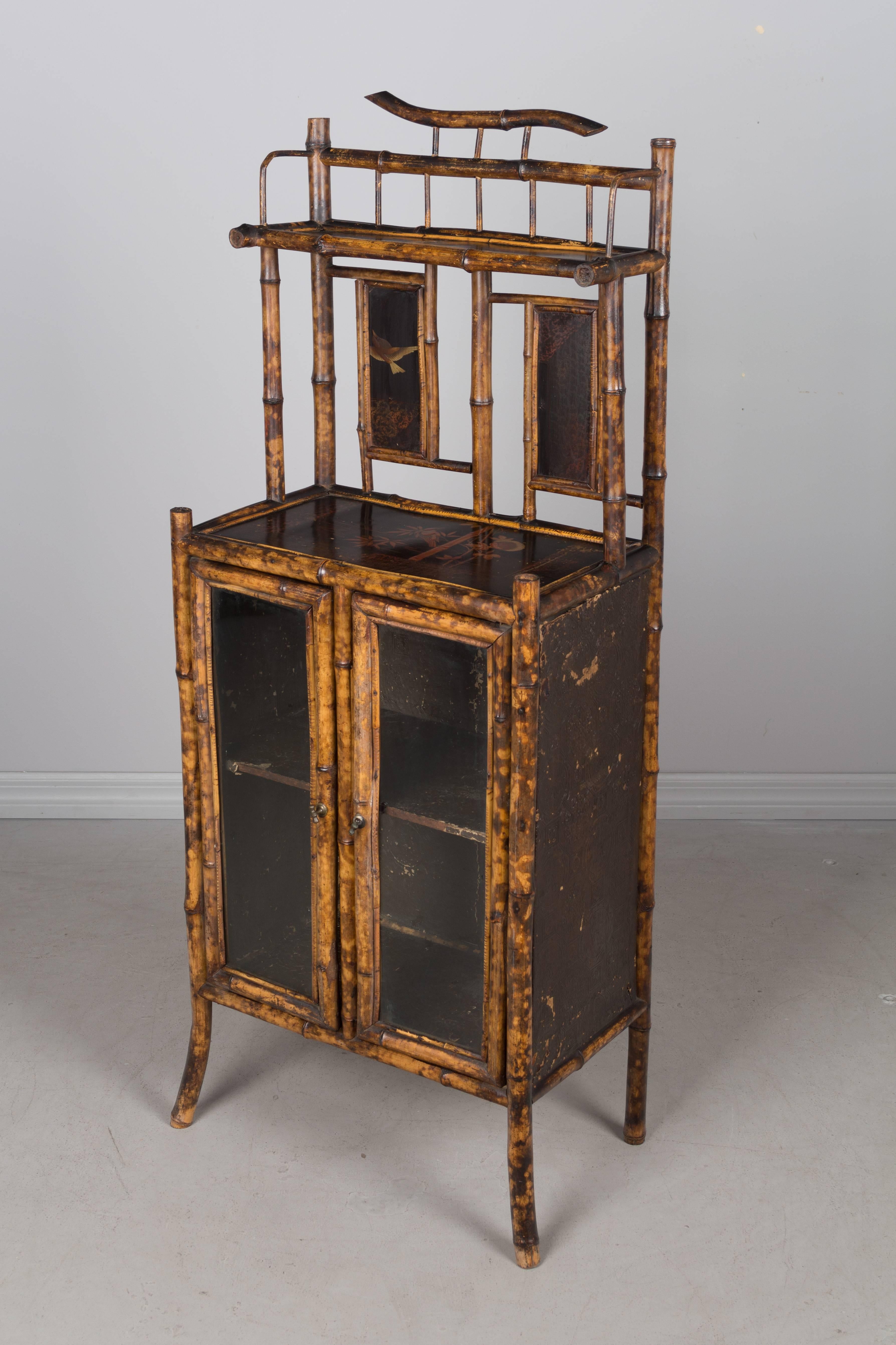 19th century English bamboo cabinet with decorative chinoiserie lacquer panels. Glass panelled doors open to one shelf. Heavy embossed paper on the sides and lining the interior. All original. Small damage to the lacquer panel of the upper