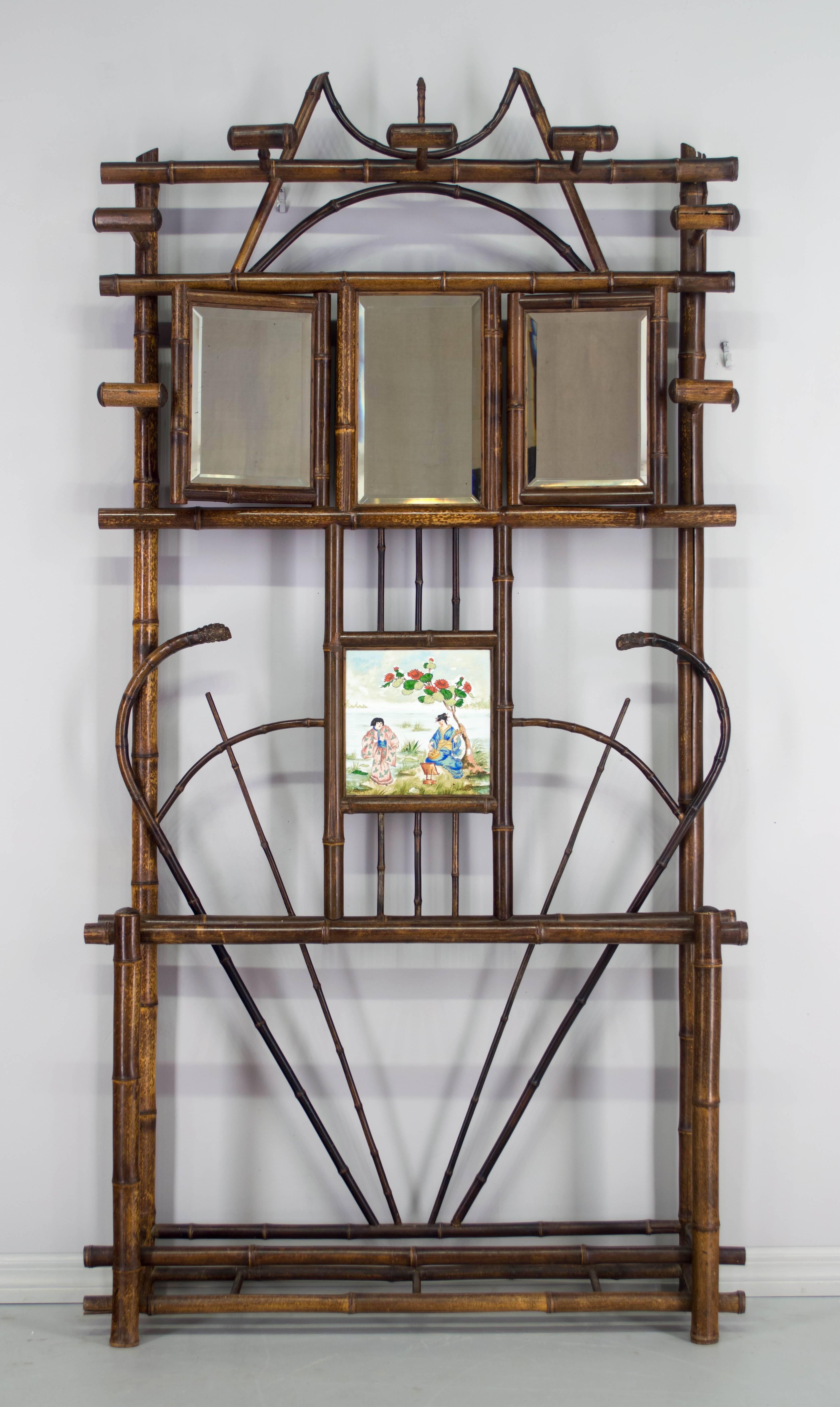 A 19th c. French bamboo hall tree with original bevelled mirrors and inset with a decorative ceramic tile, with four hooks for coats and three for hats. Plaque depicts two geishas in a pastoral scene and is stamped Montereau et Creil. We have a