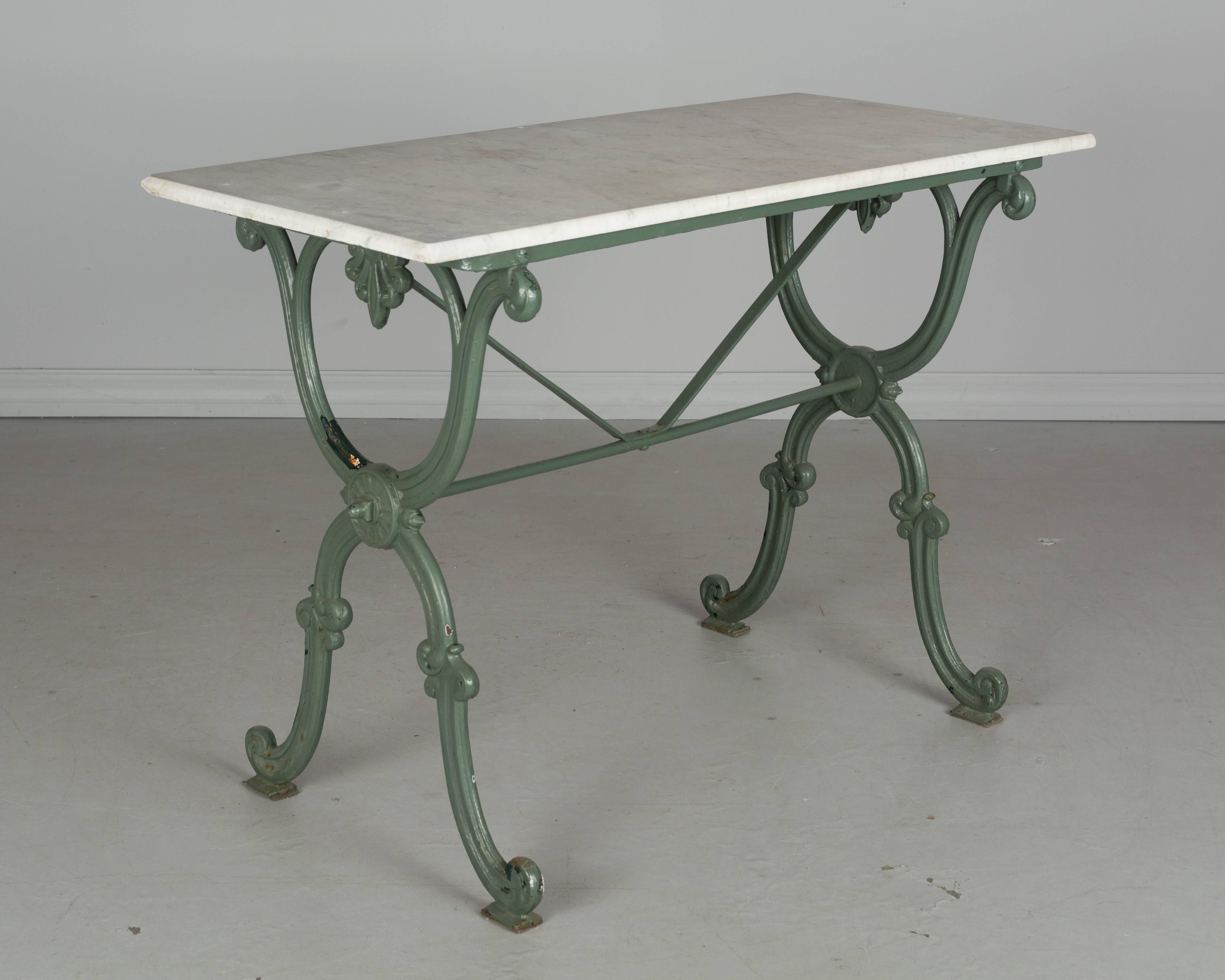 19th century French cast iron bistro table with green painted patina and marble top. Paint has chipped off a bit in a few places revealing previous paint layers of darker green and white. The marble top has been cleaned and holes have been filled