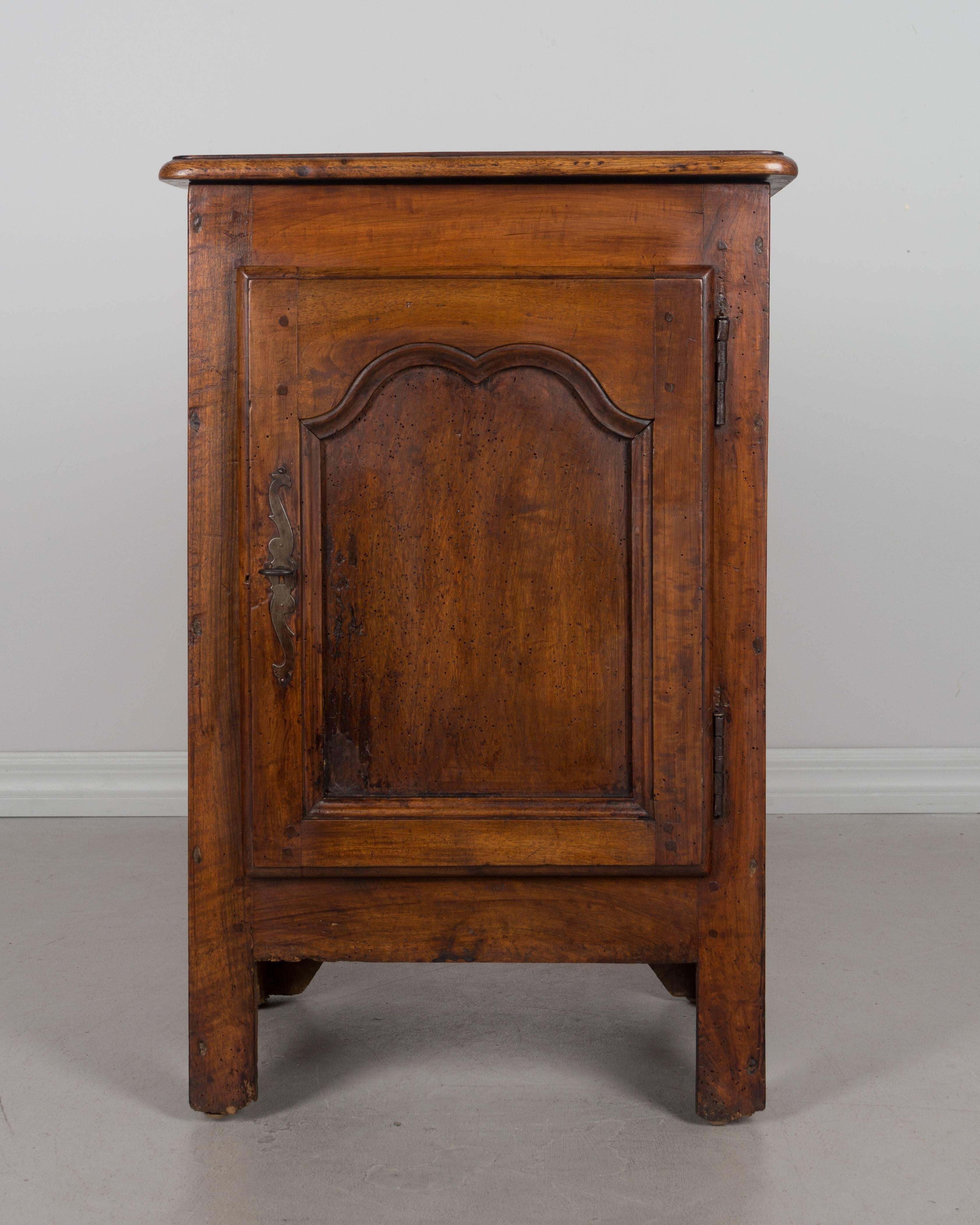 An early 19th century rustic French Country cabinet with hinged top and a door opening to a single shelf. Made of solid walnut and pine with waxed patina. Beautiful character to the wood with knots and old signs of worms that are no longer active.