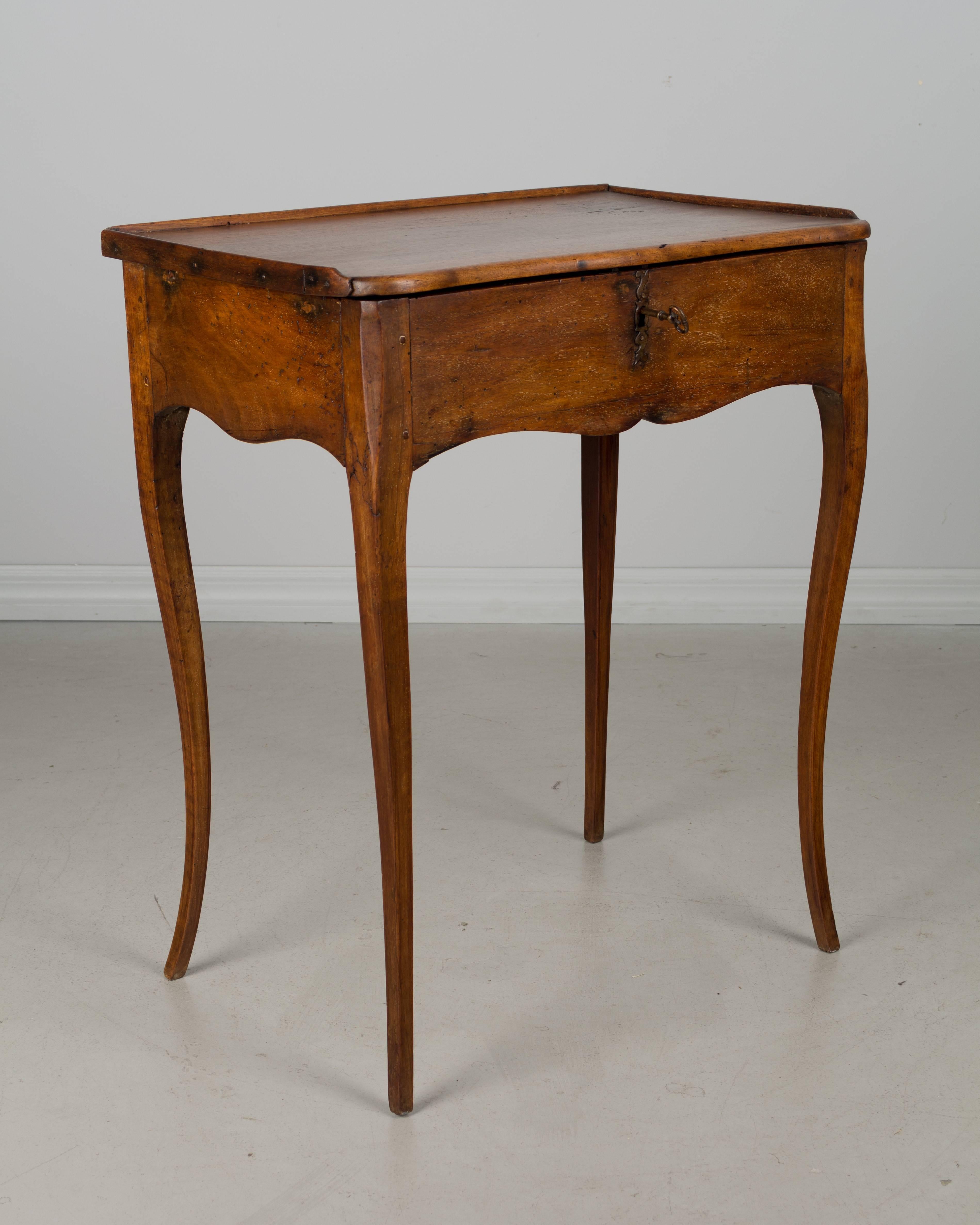 An early 19th century Louis XV style Country French side table, or work table made of solid walnut and cherry. Top hinges open to reveal divided compartments. Working lock and key. Nice proportions with slender curved legs. Restoration on back
