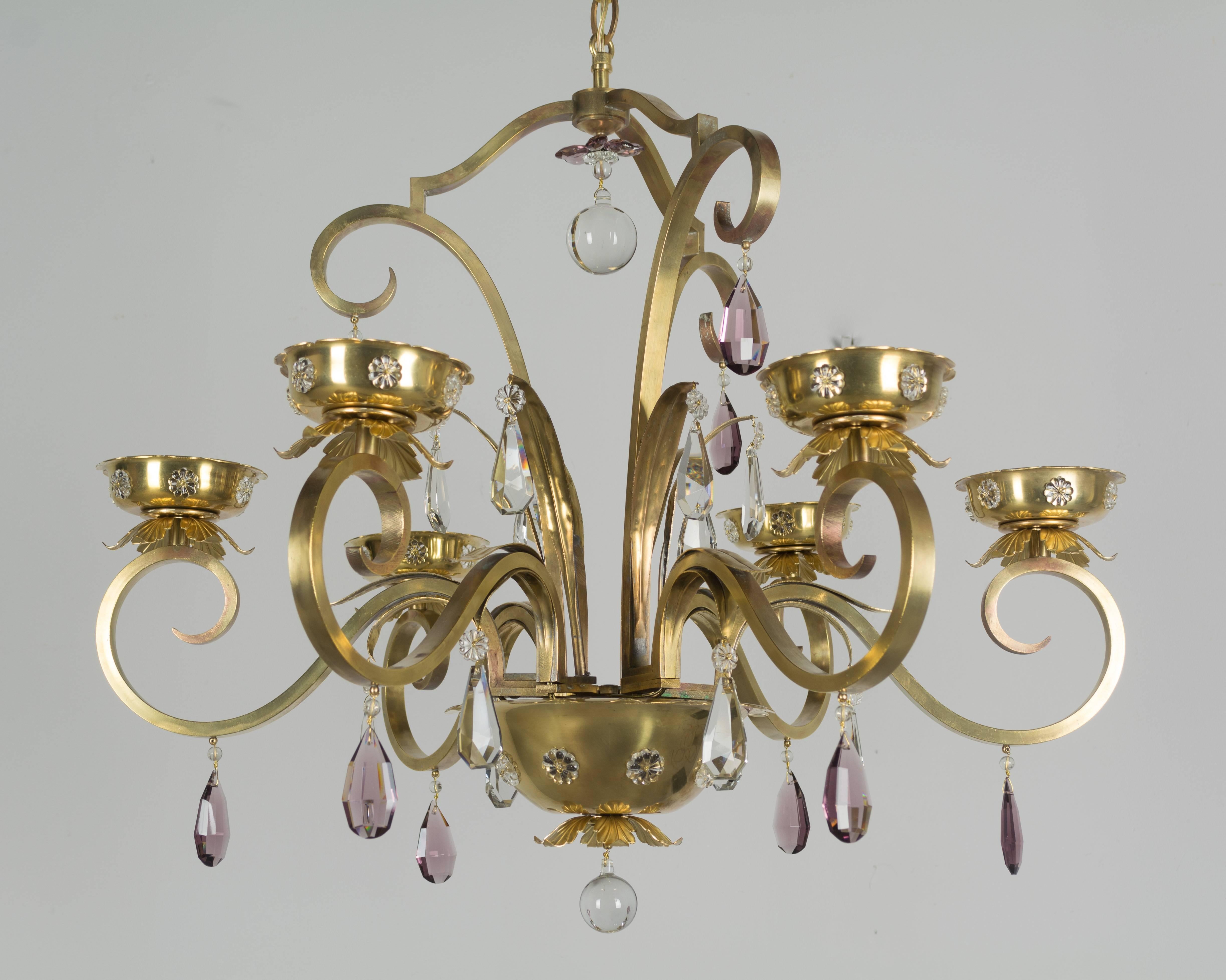 An unusual French Modern six-arm chandelier  style of Maison Jansen. Light shines through perforated brass dome and candle cups creating a dramatic effect when lit. Decorated with clear and amethyst faceted crystal prisms and rosettes. Polished
