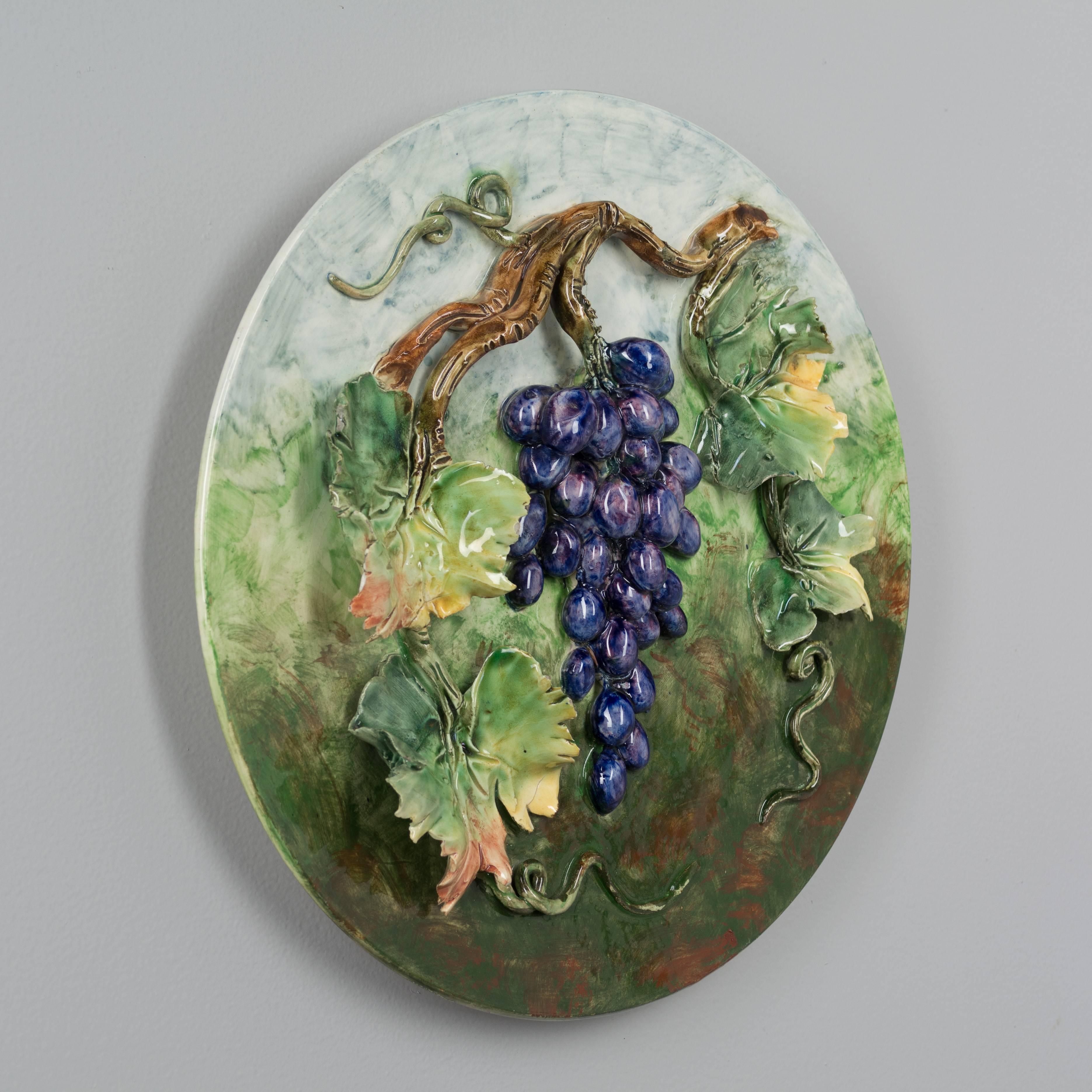 A 19th century French Barbotine Majolica wall platter with a bright purple grape cluster hanging from a vine with four large leaves and tendrils. Sculpted in high relief and hand-painted in vivid color. Stamped on back: Longchamp Terre de Fer.