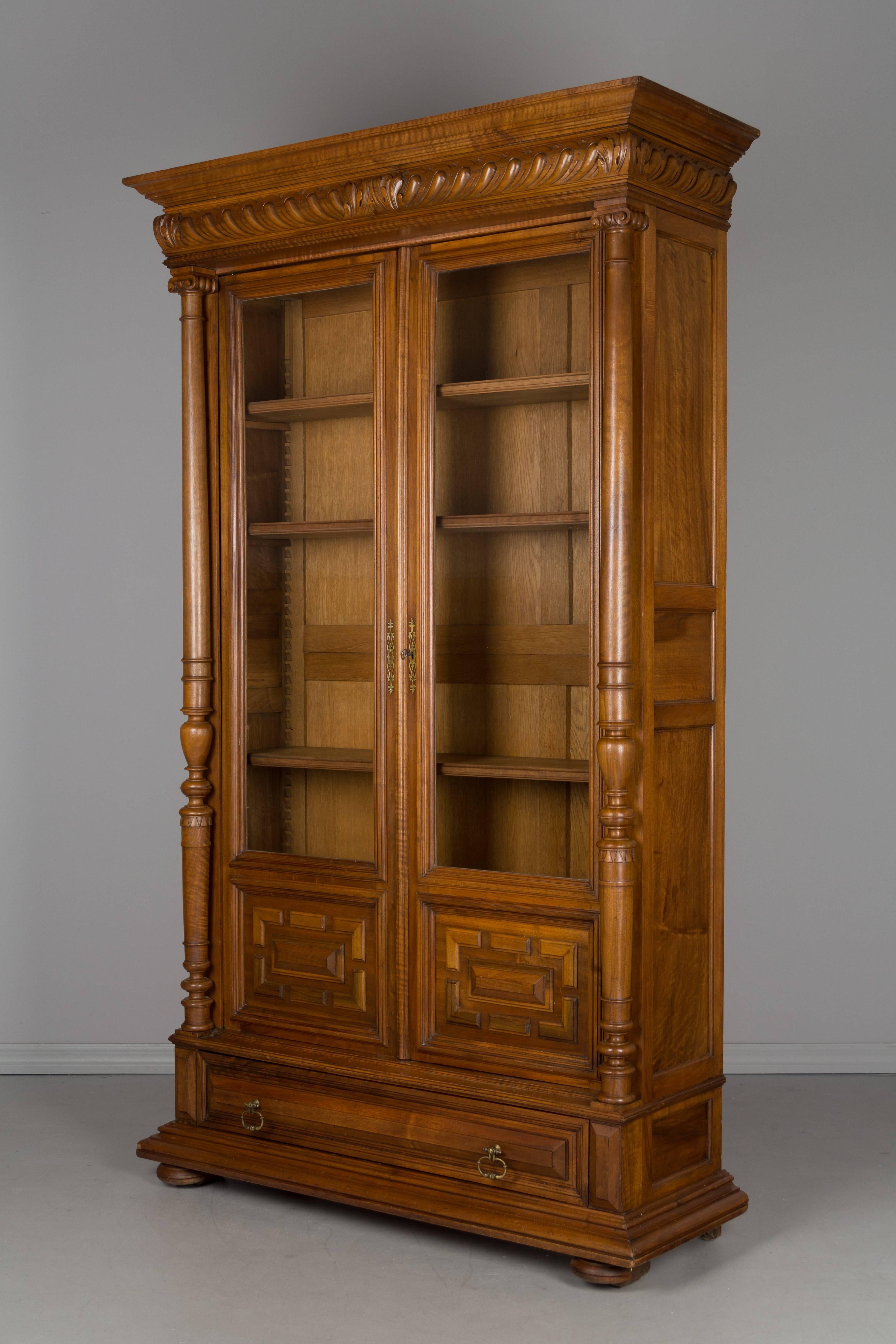 A 19th century, French Henri II style bibliotheque, or bookcase, made of solid walnut with fine carved details and turned columns. Single dovetailed drawer at the bottom with original brass pulls. Original glass paned doors with working lock and