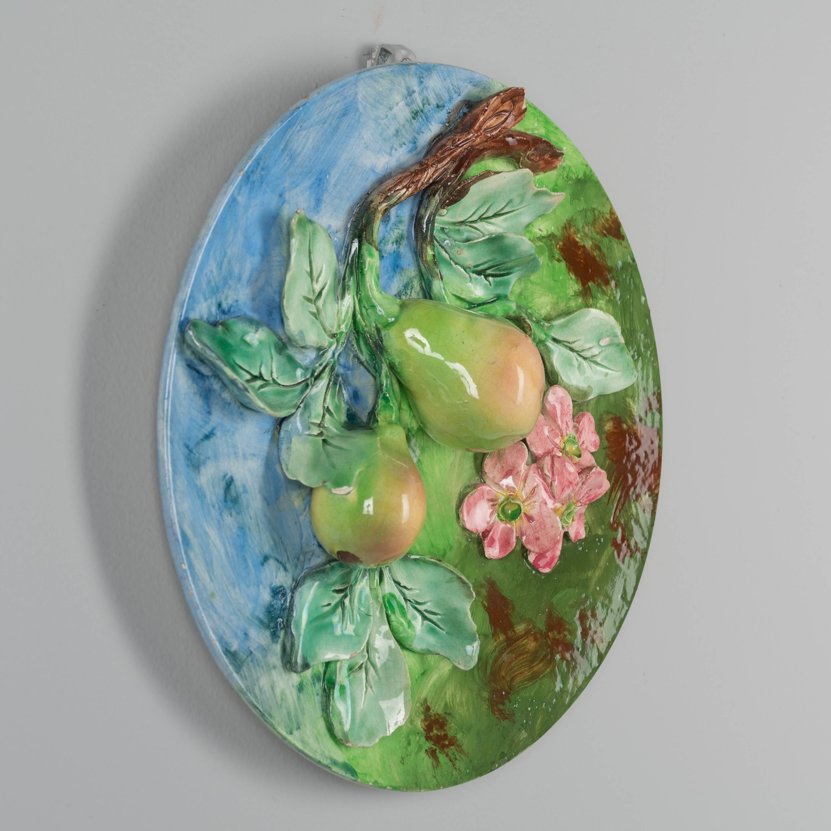 A 19th century French Barbotine Majolica wall platter with two pears hanging from a tree branch with green leaves and pink blossoms. Sculpted in high relief and hand-painted in vivid color. Stamped on back Longchamp Terre de Fer. Chips and losses to