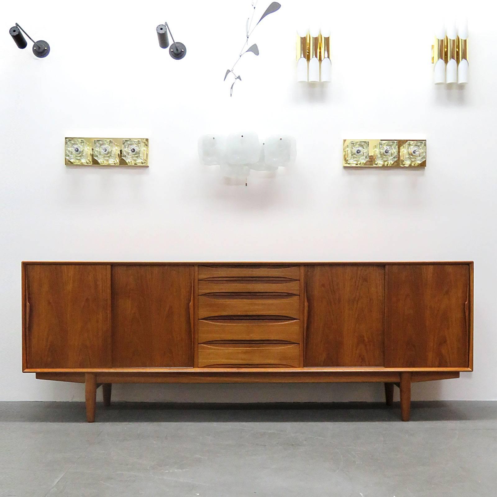 Wonderful long Danish teak sideboard by Dyrlund/Smith A/S with two shelves on either side behind double sliding doors with sculptural handles, five center drawers with sculptural fronts, the top three padded with green felt and various silverware