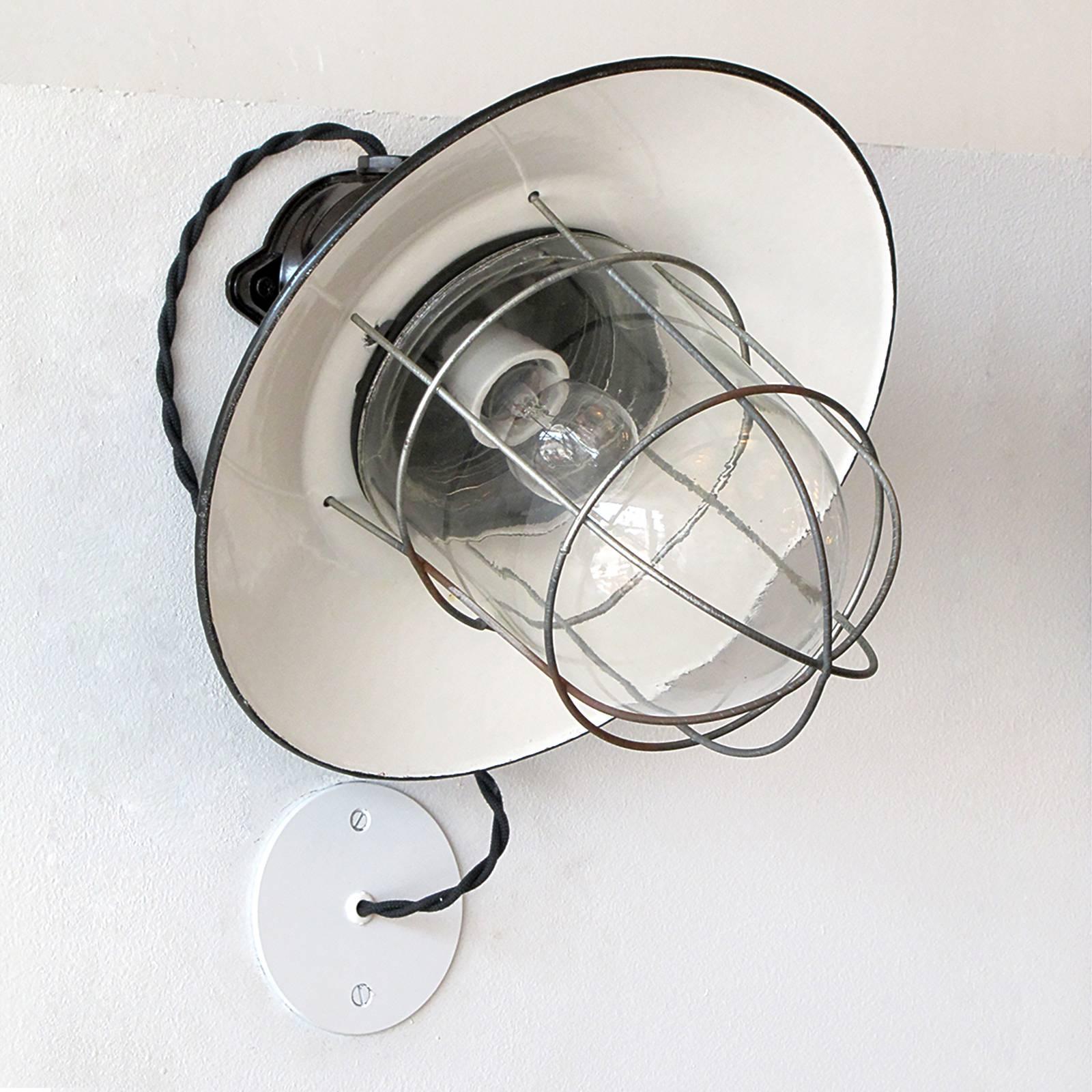 Great pair of German Industrial wall lights with bakelite housings, enameled metal shades and a metal cages enveloping glass domes, currently wired with external j-box covers.