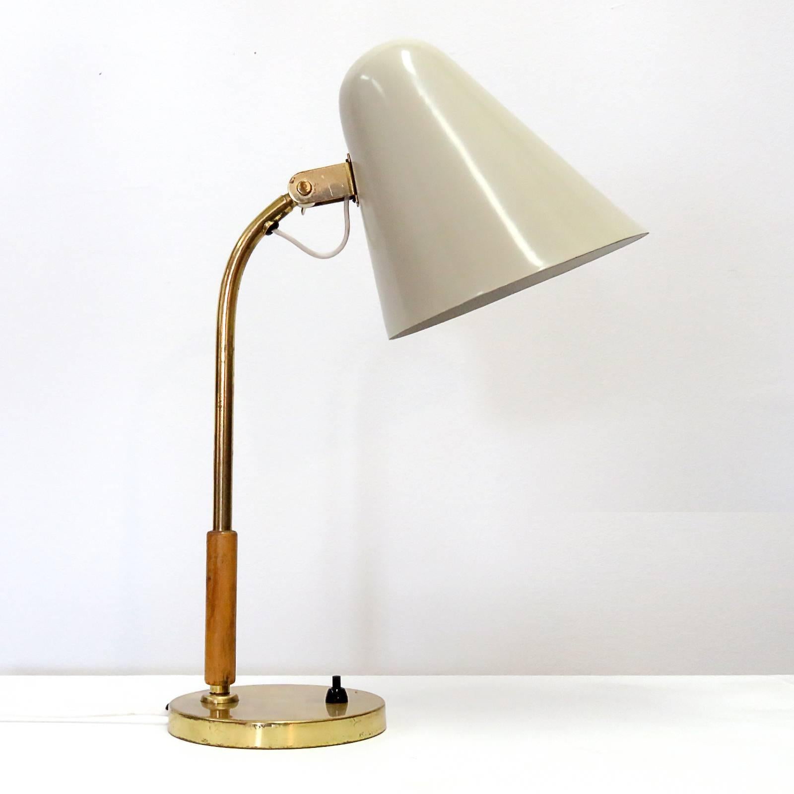 Wonderful desk lamp by Paavo Tynell for Taito, Finland, with large articulate crème colored enameled shade, wooden handle and brass arm and base, signed OY Taito.