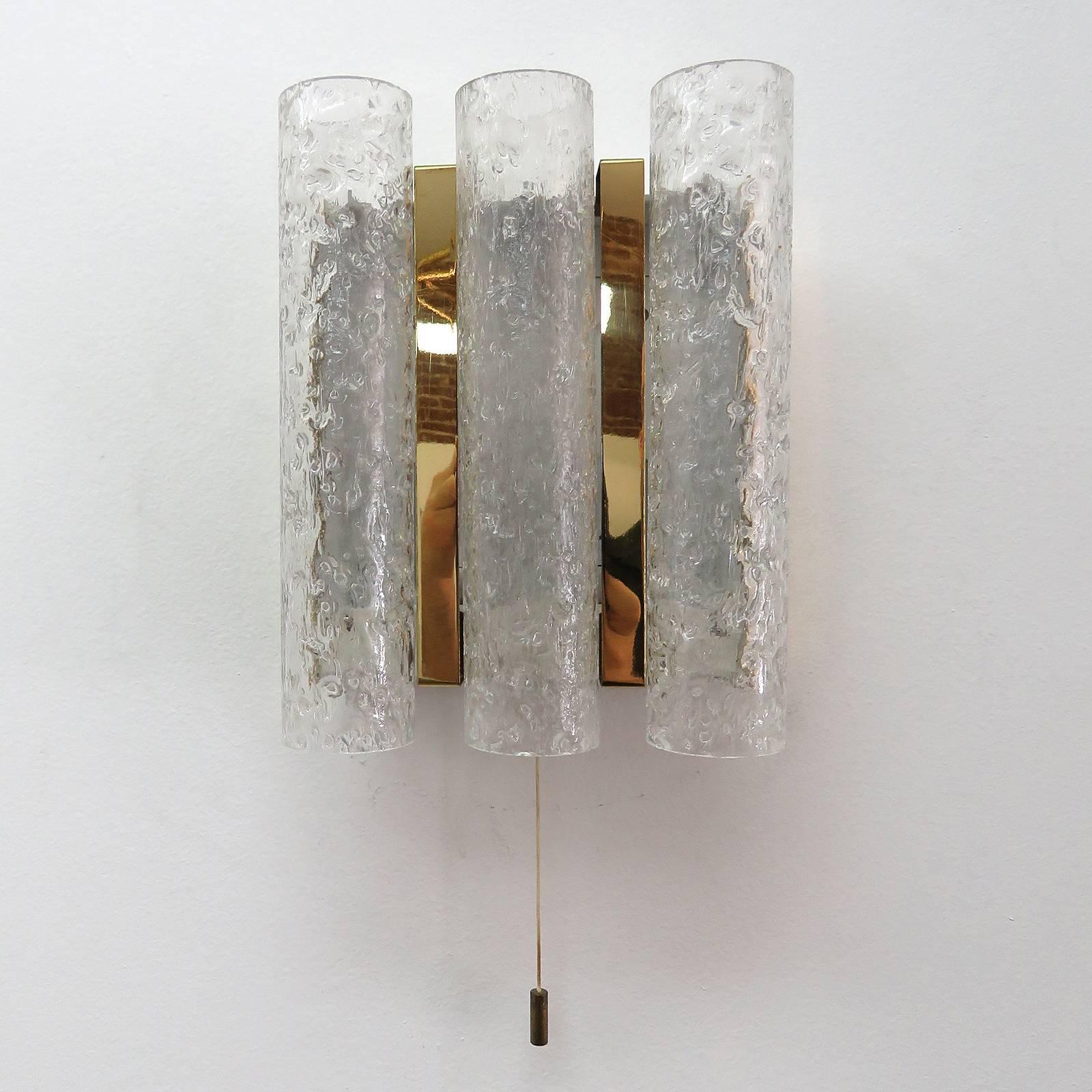 Wonderful pair of 1960s wall lights by Doria with three hanging cylinders of textured ice glass separated by brass details. Each fixture carries two candelabra sockets and a pull string on/off switch.