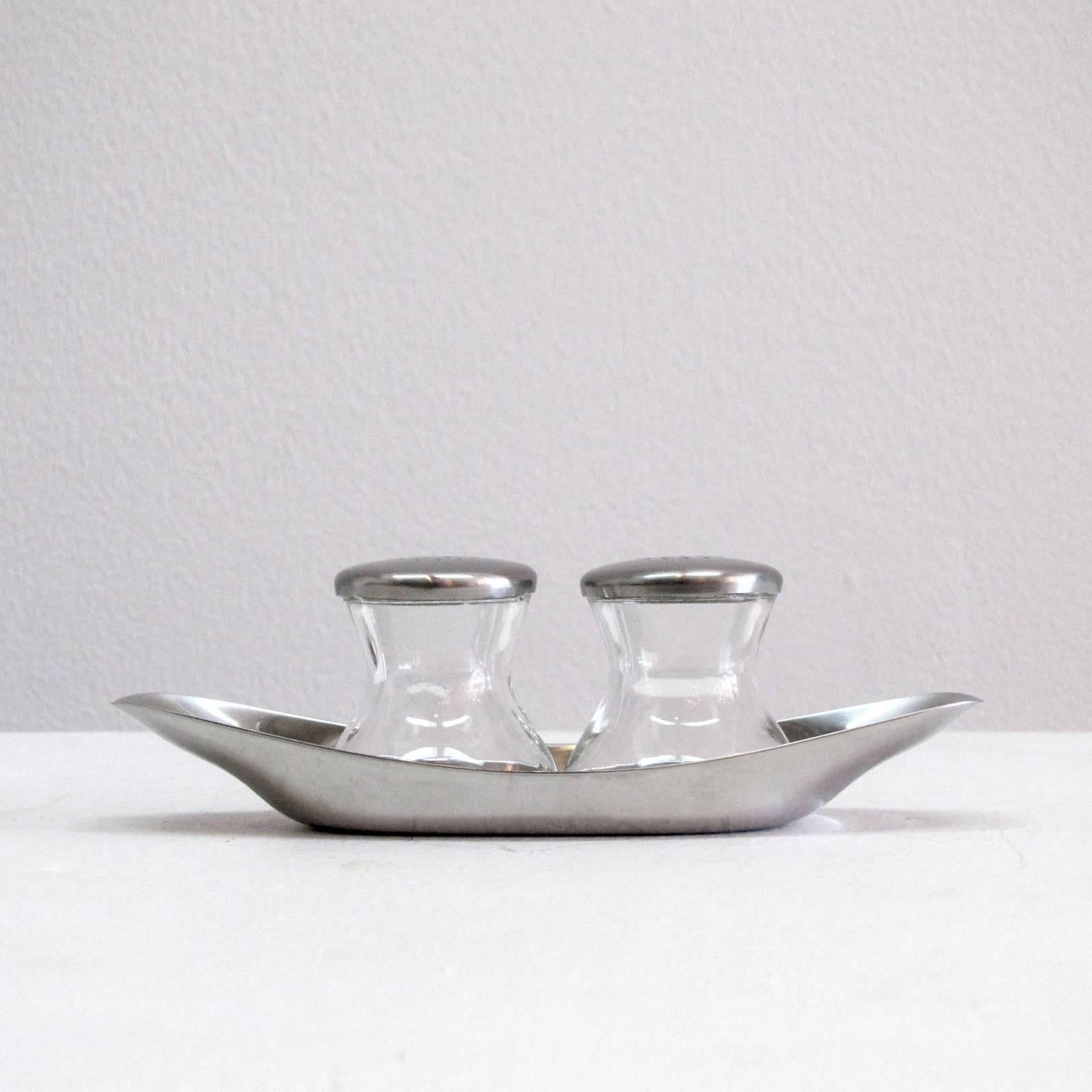 Classic, complete salt and pepper shaker set by Wilhelm Wagenfeld for WMF, WV 505. The set includes two pressed glass shakers with perforated lids and a cromargan (stainless steel derivative) plate or holder, part of the MoMA permanent collection.