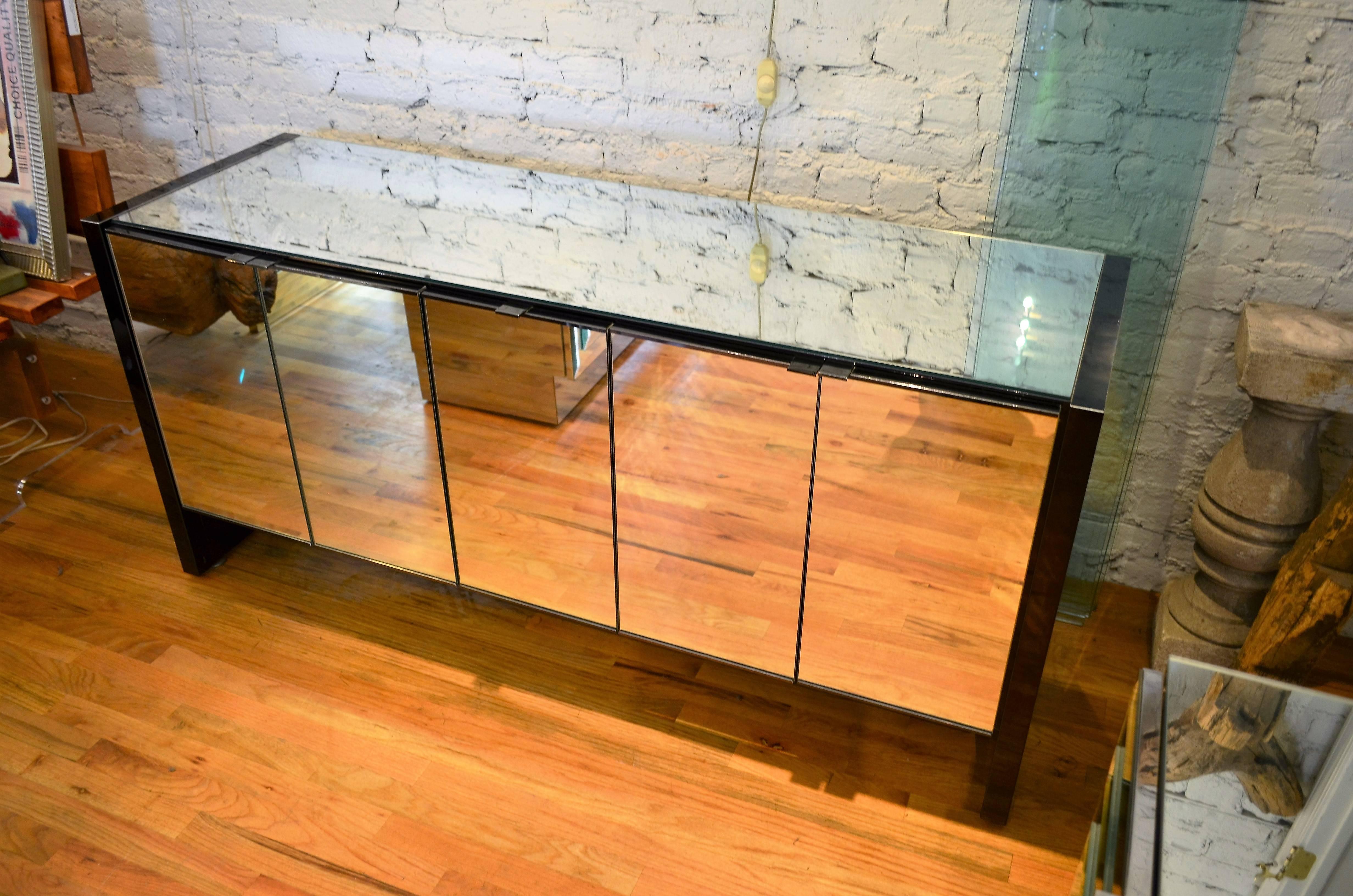 An outstanding and rare example of Ello's iconic Mid-Century mirrored credenza.
The piece features mirrored doors and top accented with black chrome sides, trim and pulls.
Three compartments each contain an adjustable shelf. A highly versatile