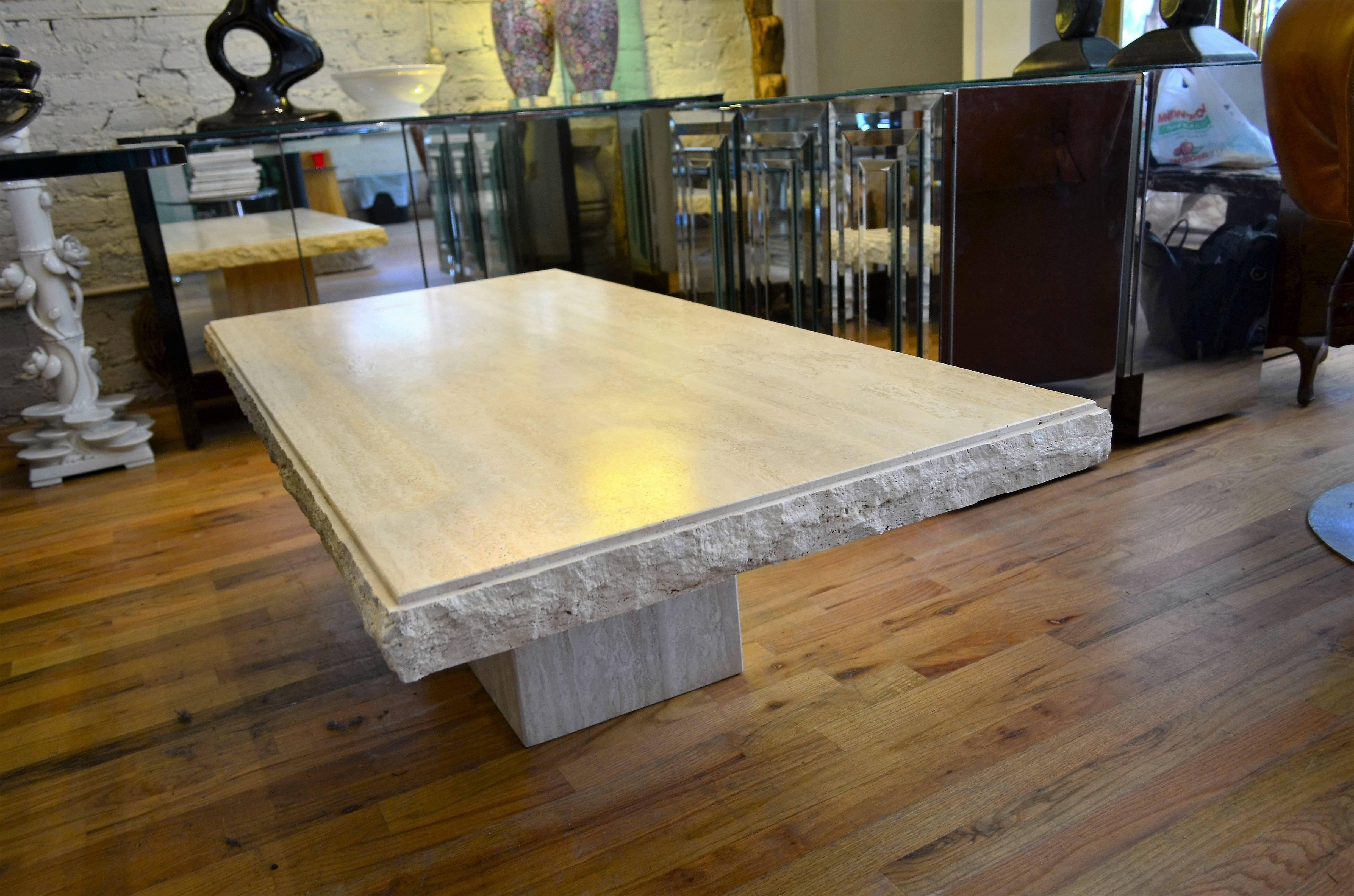 A large Mid-Century polished travertine coffee table.
This coffee table is substantial and rests on a pedestal base.
The top is richly veined with a pronounced rusticated edge.